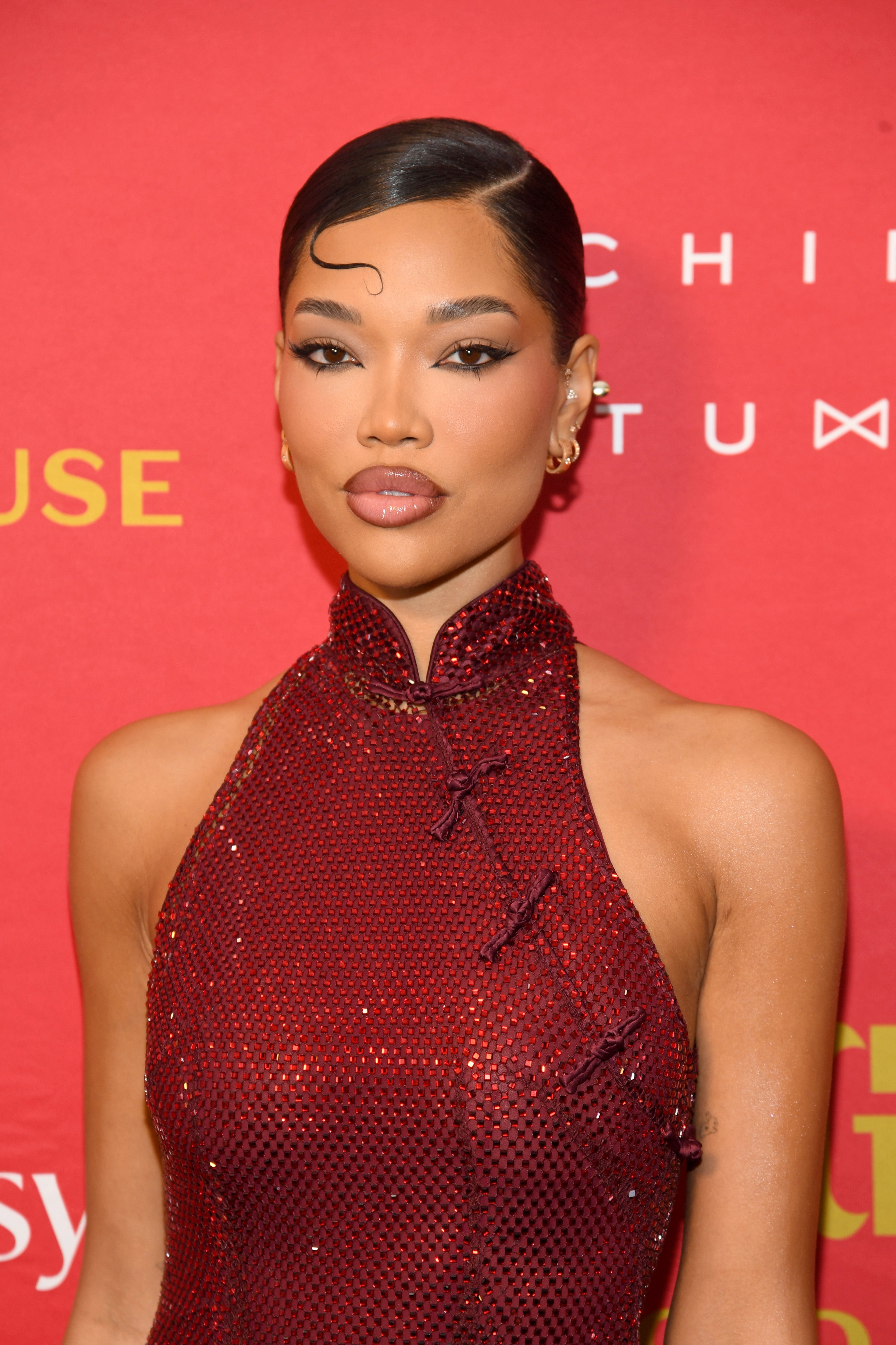 Person successful  a sleek, sleeveless high-neck outfit with a textured pattern, attending a reddish  carpet lawsuit   with a blase  hairstyle