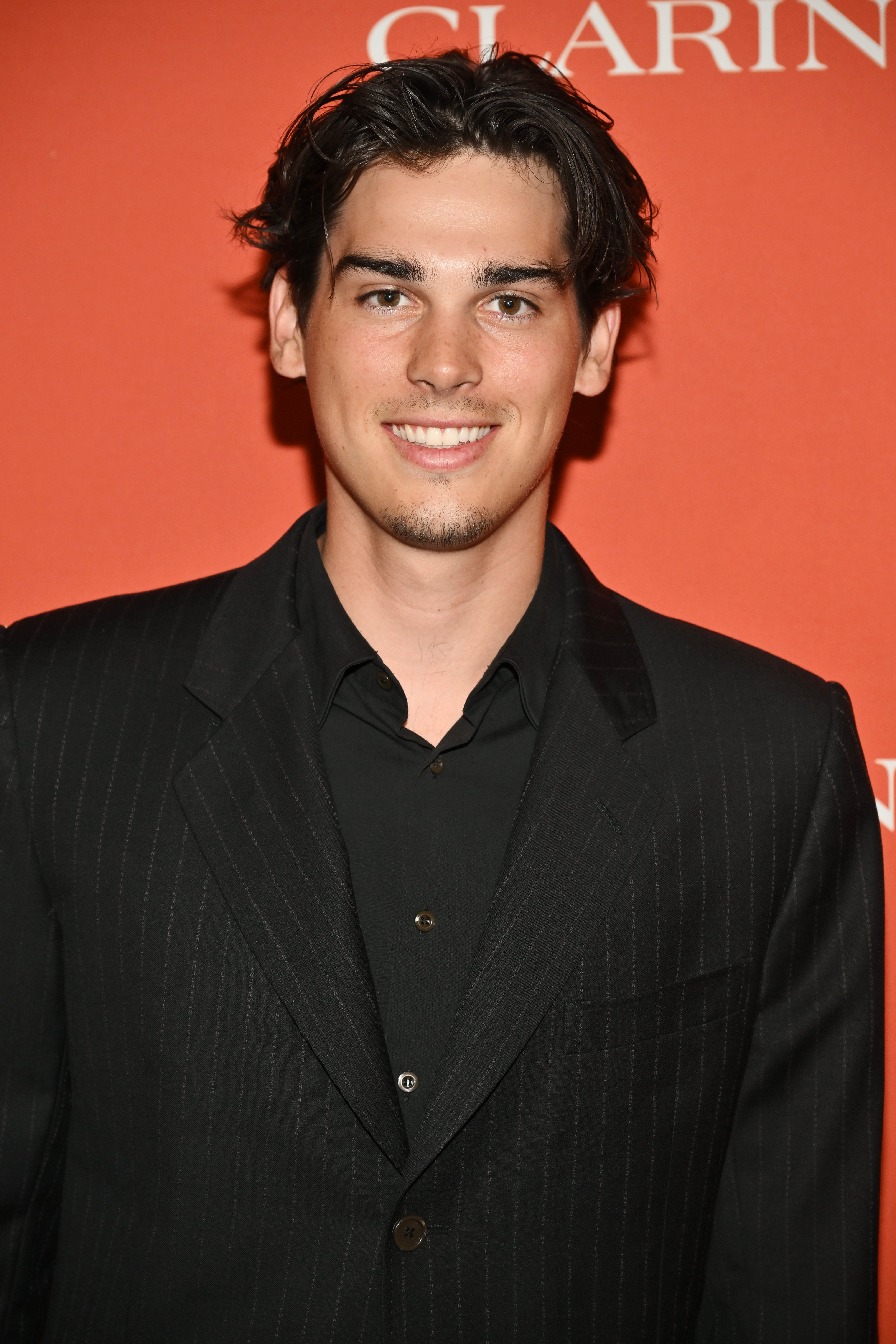 Person astatine  a personage  lawsuit   successful  a classical  pinstripe suit, smiling successful  beforehand   of an lawsuit   backdrop