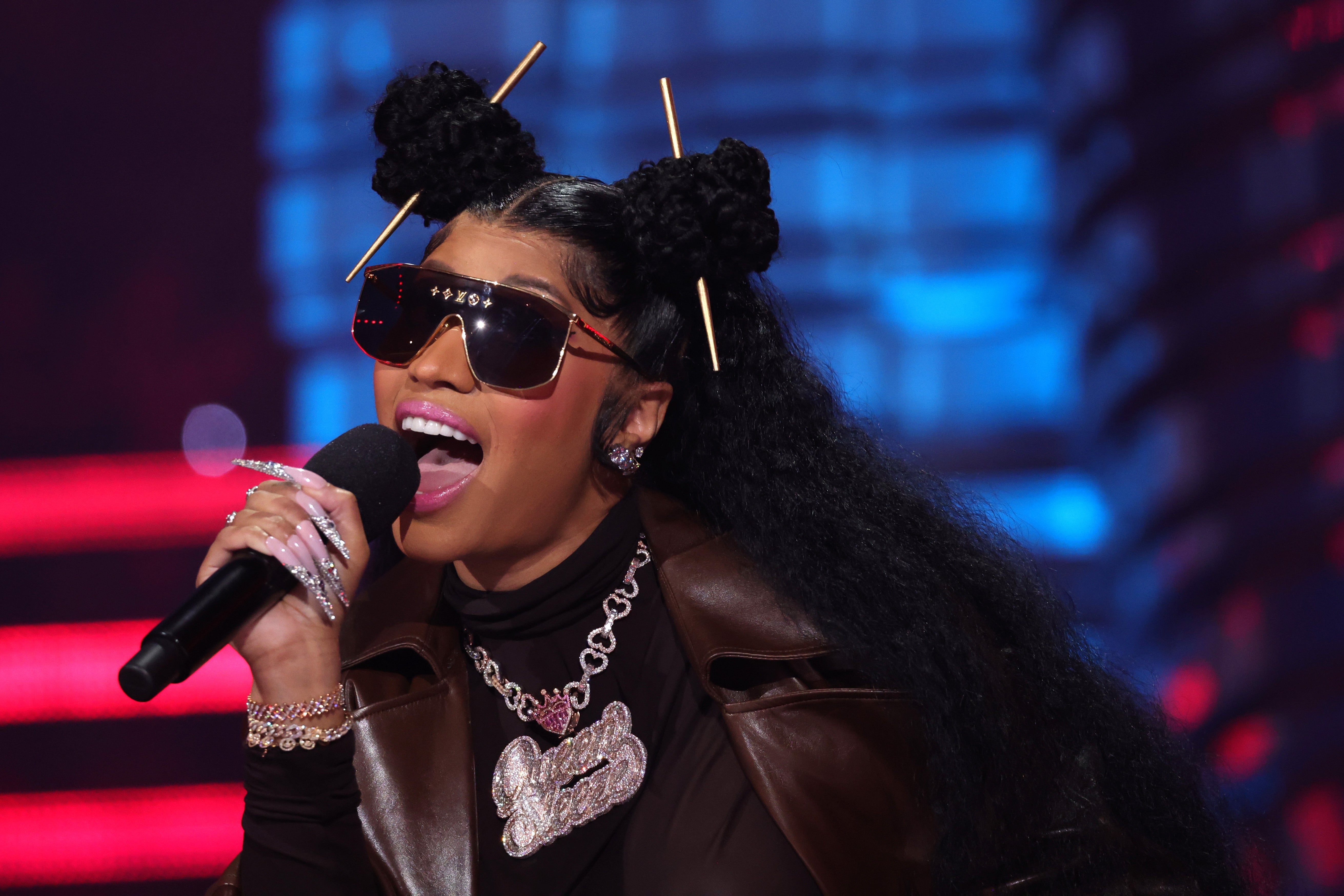 Nicki Minaj performs connected signifier wearing sunglasses, a leather jacket, and connection jewelry, with hairsbreadth styled successful buns held by sticks
