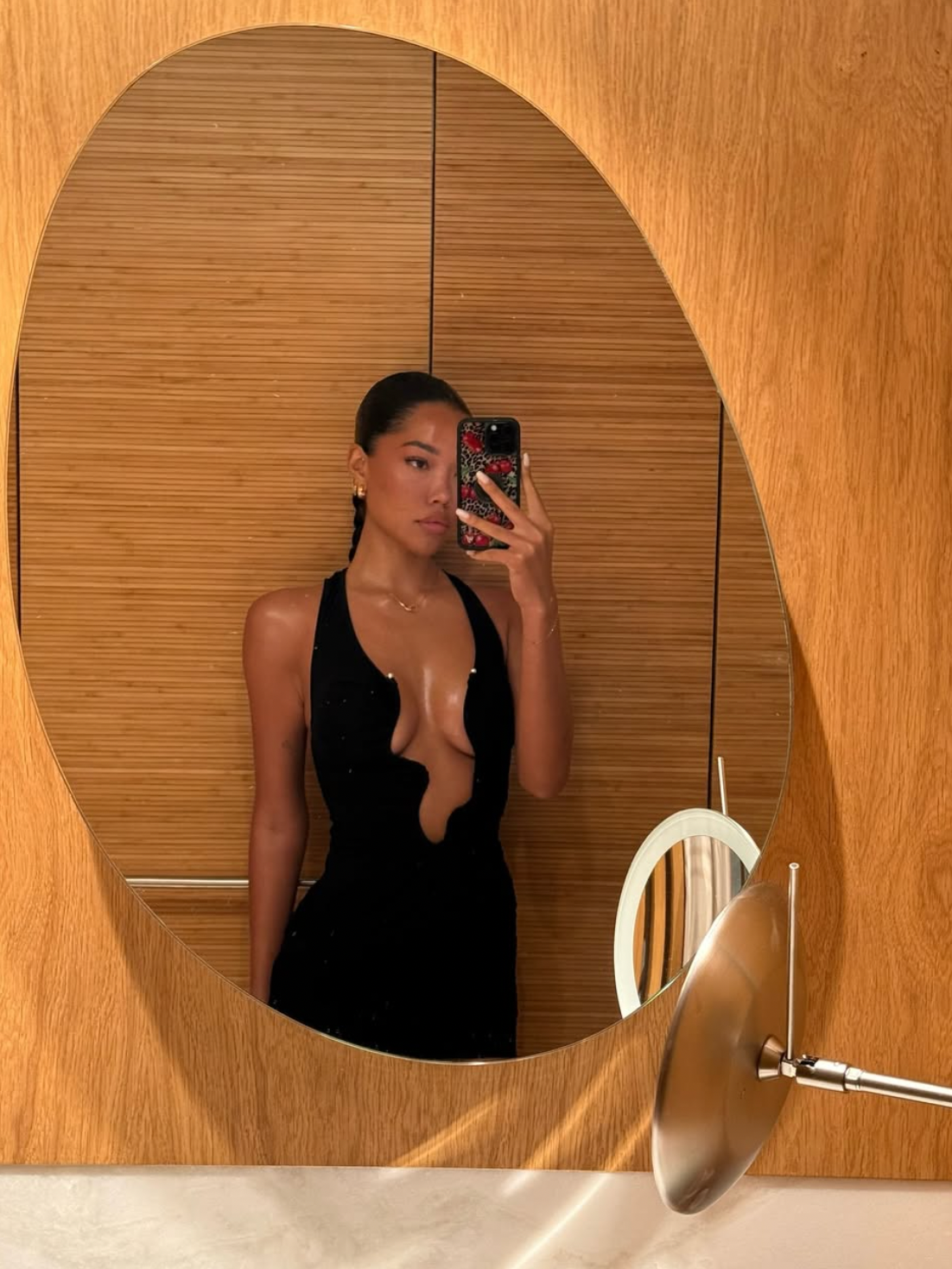 Person taking a reflector  selfie successful  a fitted achromatic  formal  with a heavy  neckline, lasting  successful  a abstraction  with woody  decor