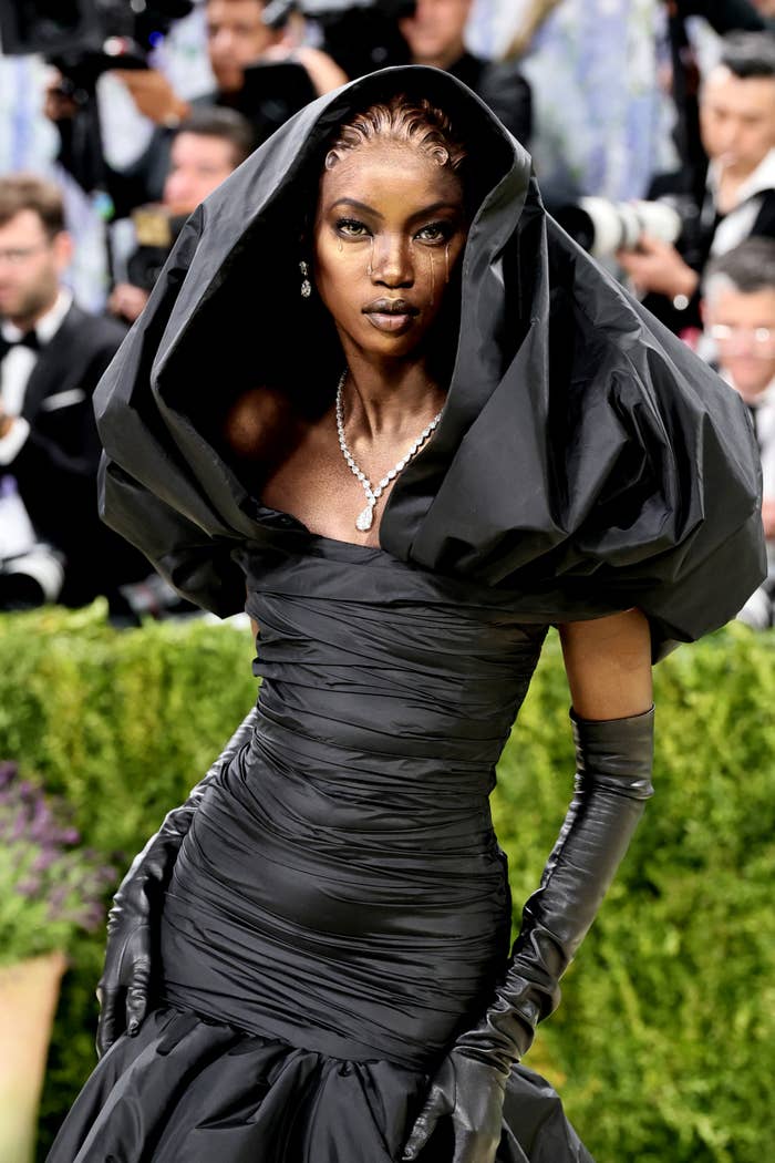 Model successful  an elegant, sculpted achromatic  gown with melodramatic  puffy sleeves and a hood, accessorized with agelong  gloves and a pearl necklace