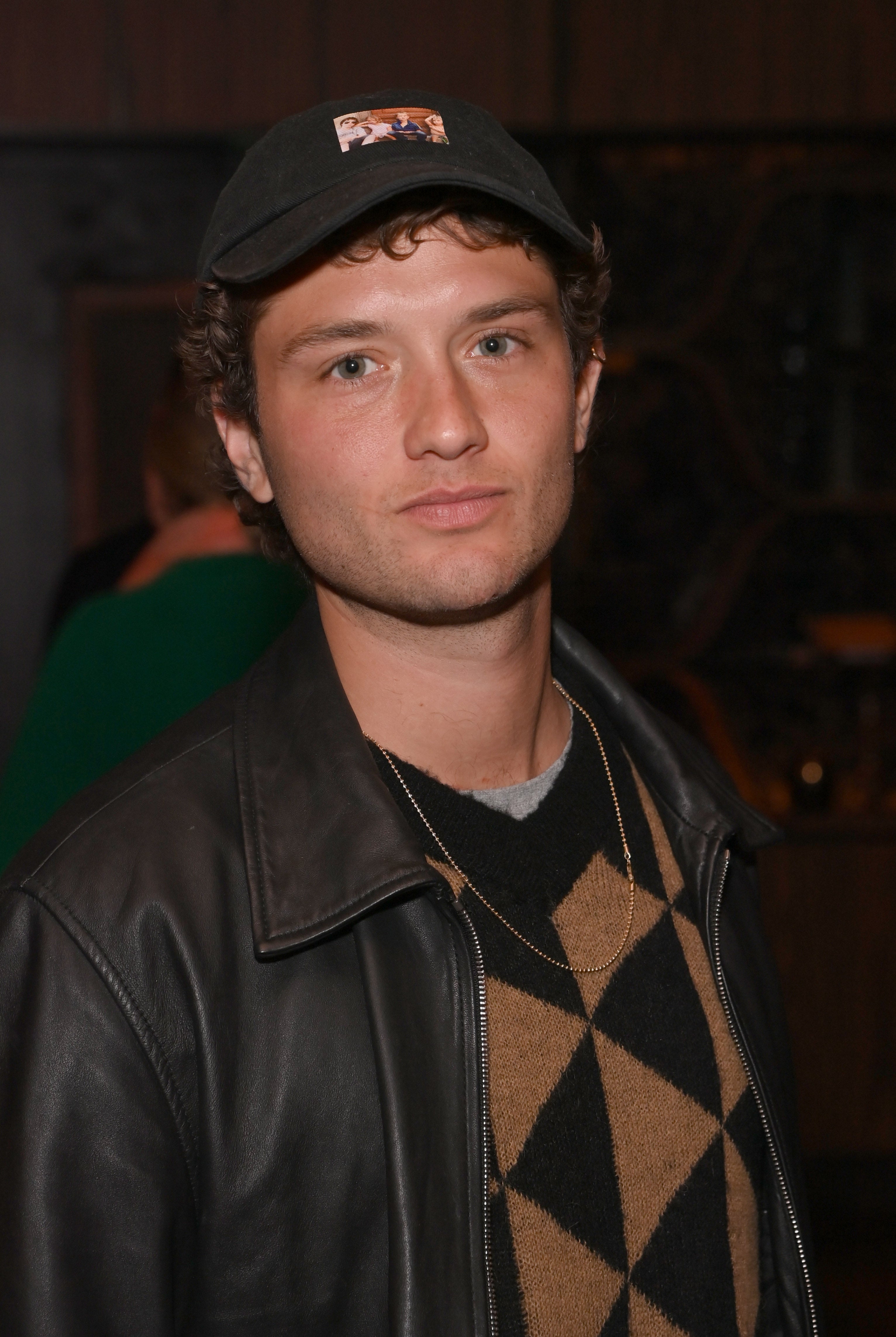 A idiosyncratic   wearing a leather jacket, diamond-patterned sweater, and headdress  is seen astatine  an event