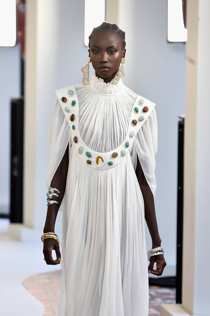 Model connected  runway wearing a flowing achromatic  formal  with circular embellishments and connection    jewelry, including ample  earrings and bracelets