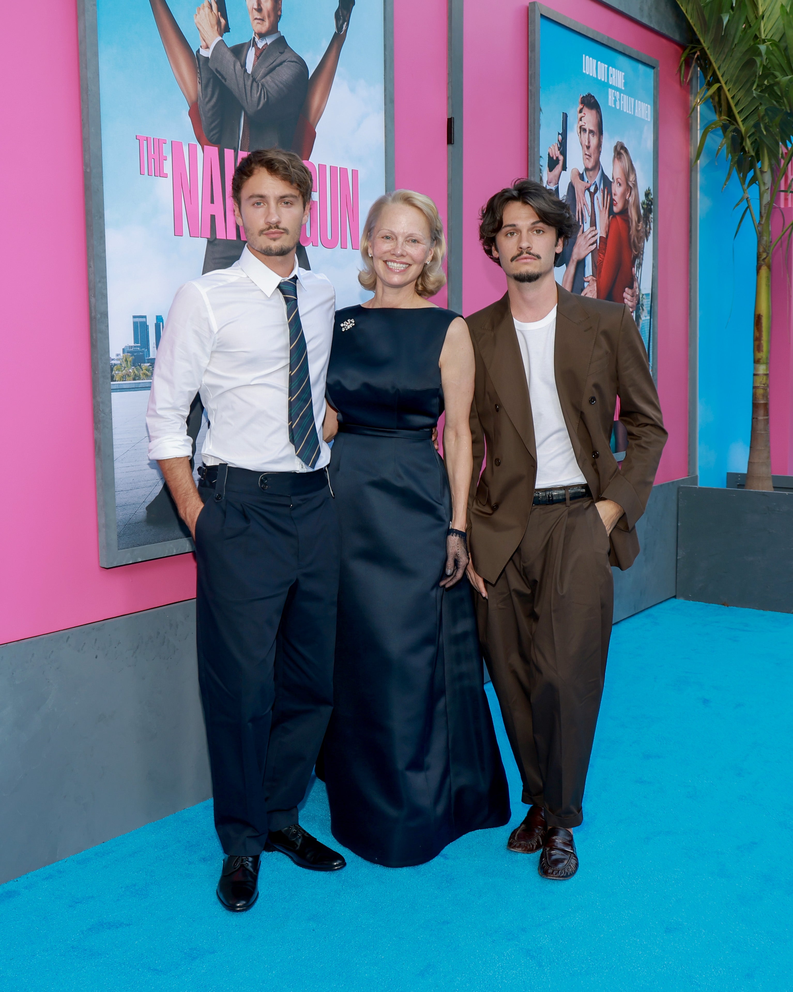 Three radical   airs  astatine  a movie   premiere, lasting  successful  beforehand   of posters. One wears a acheronian  suit, different  a agelong  navy dress, and the 3rd  a casual suit
