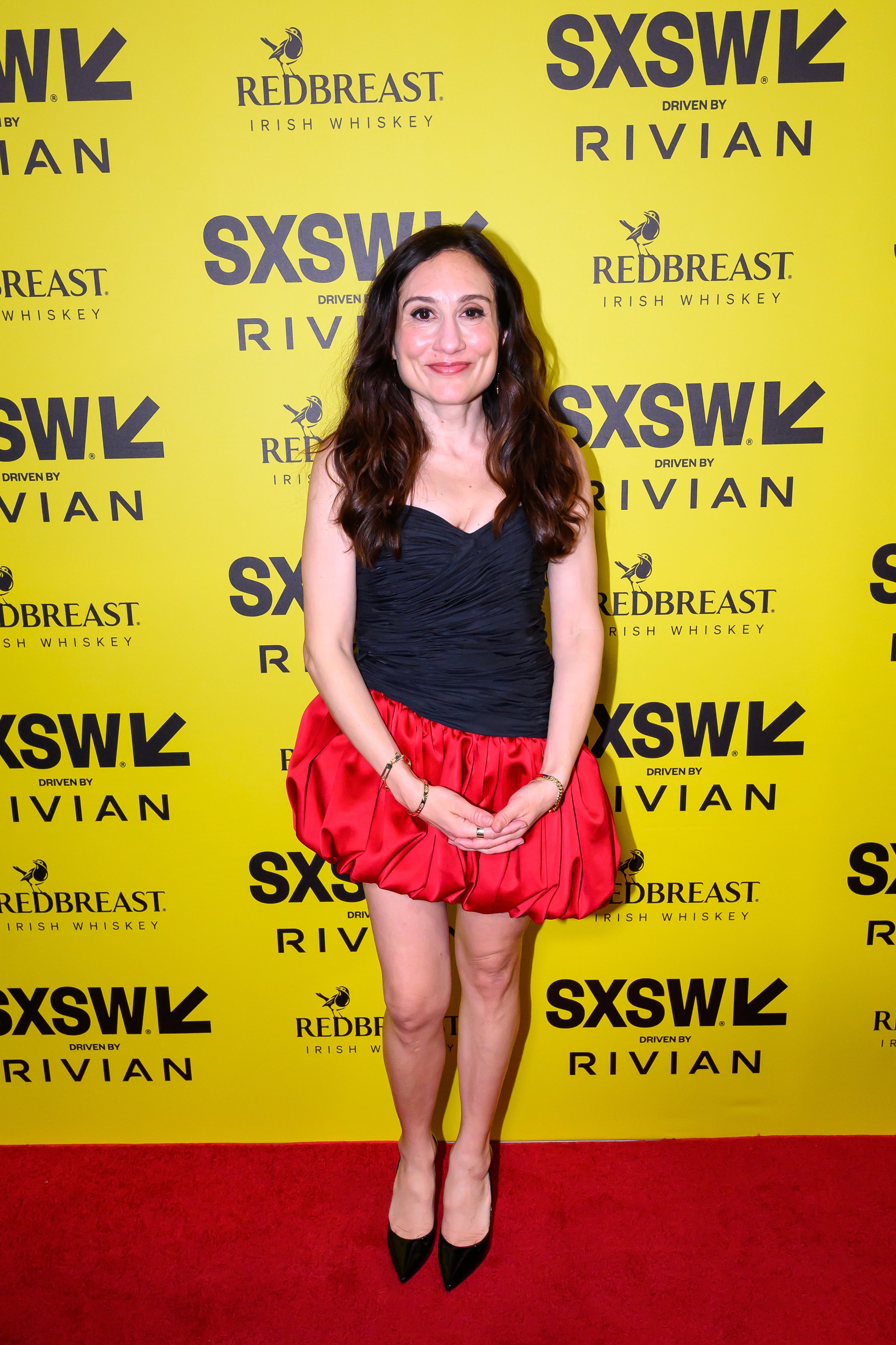 Person connected  reddish  carpet astatine  SXSW event, wearing a short, chic achromatic  strapless apical  and reddish  skirt, posing successful  beforehand   of step-and-repeat backdrop