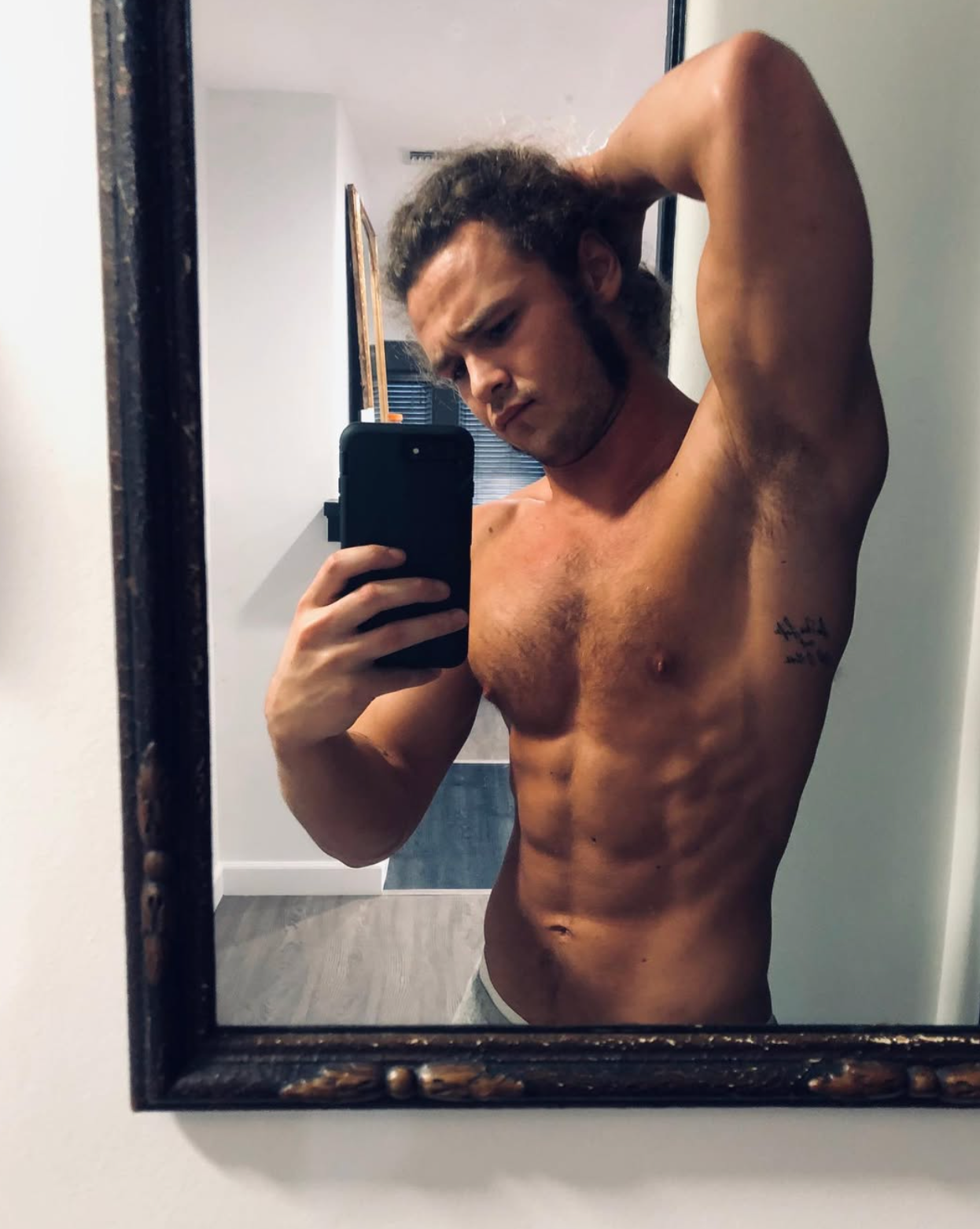 A idiosyncratic   takes a reflector  selfie, shirtless, posing with 1  limb  flexed down  their head