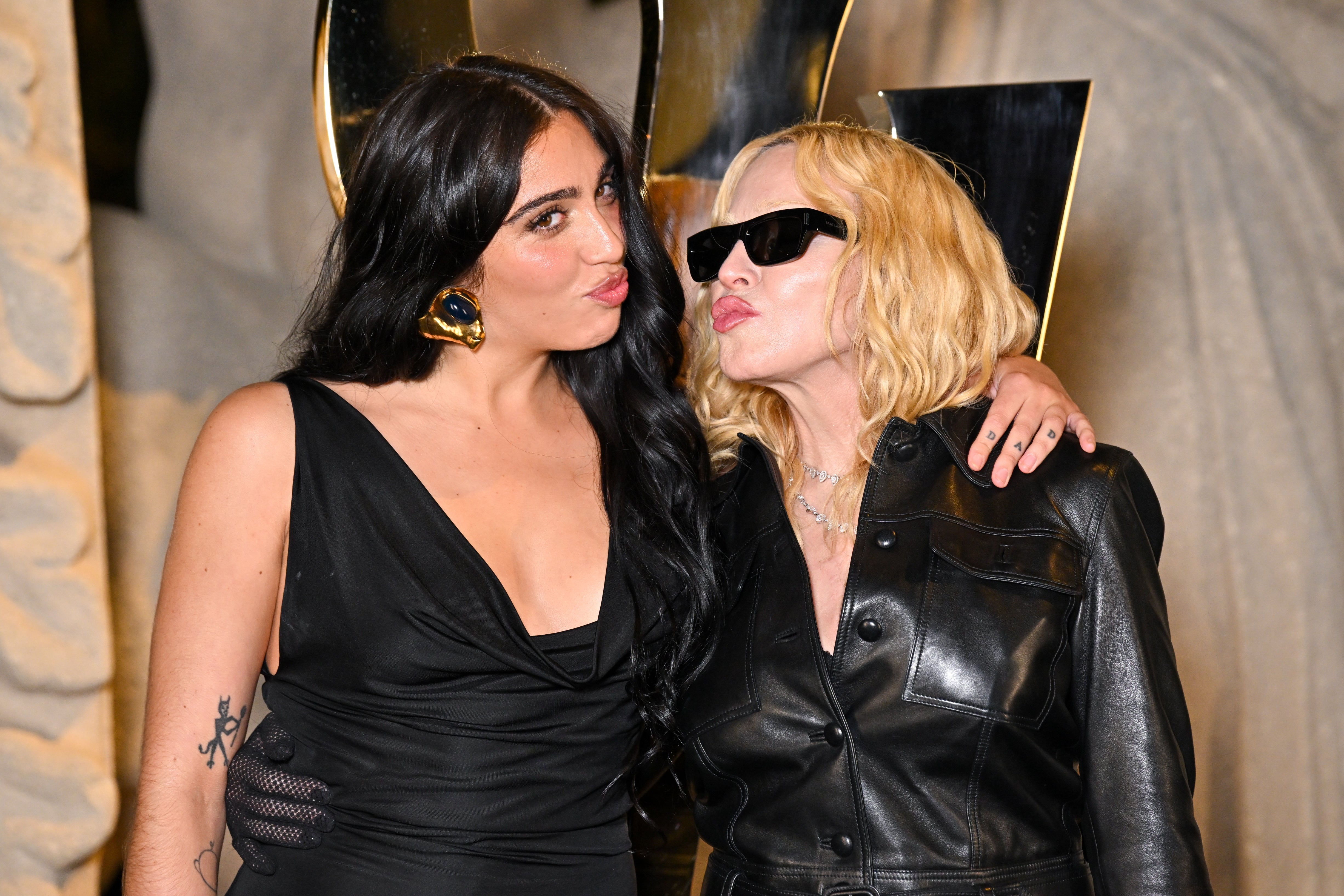 Two radical   posing together, 1  successful  a achromatic  formal  with enarthrosis  tattoo, the different   successful  a achromatic  leather overgarment   and sunglasses, broadside  by side