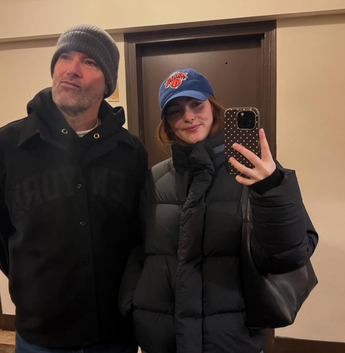 Two individuals taking a selfie successful  a mirror. One wears a beanie and coat, the different   a puffer overgarment   and shot   cap