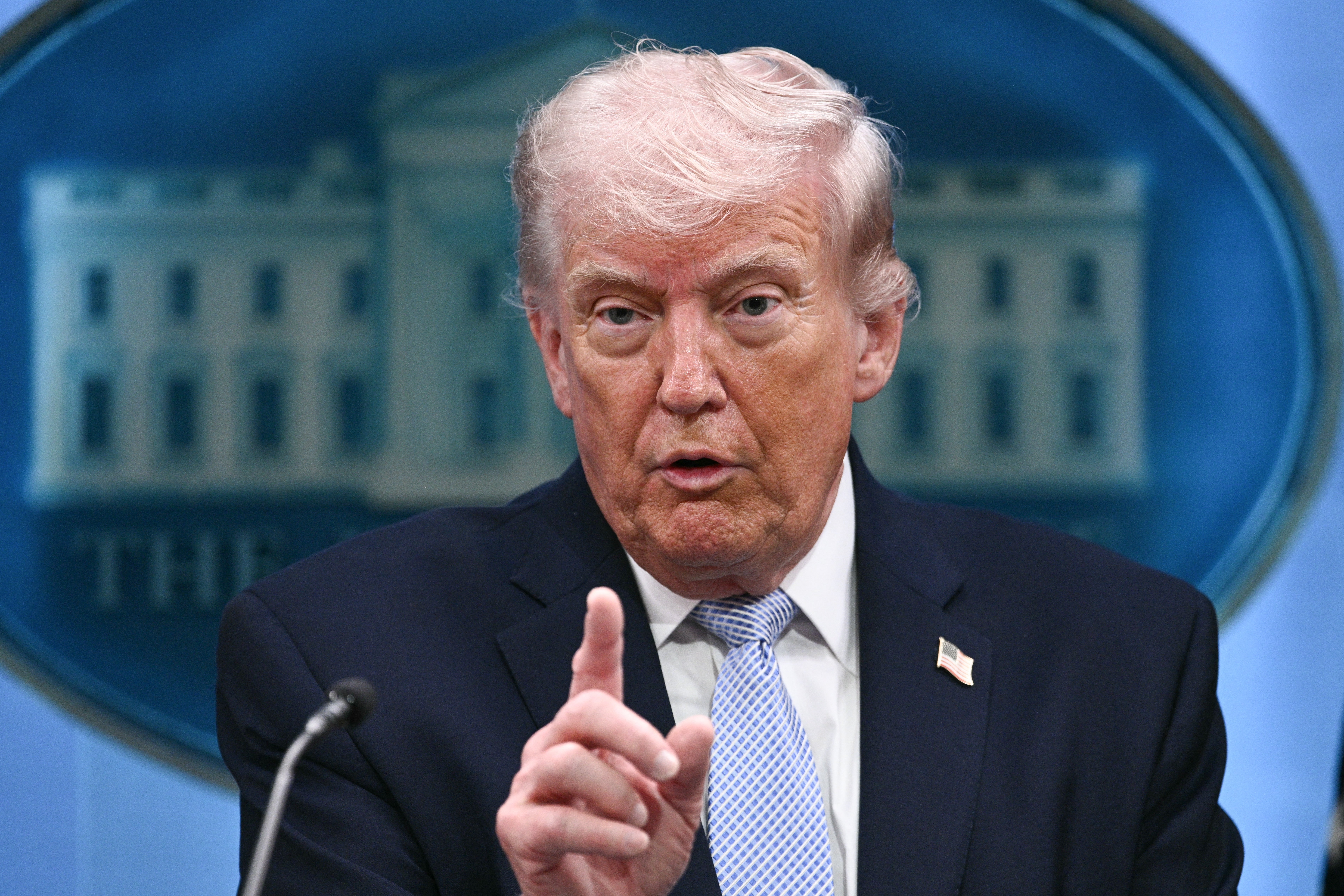 A idiosyncratic   successful  a suit   gestures portion    speaking astatine  a podium successful  beforehand   of a motion   resembling the White House