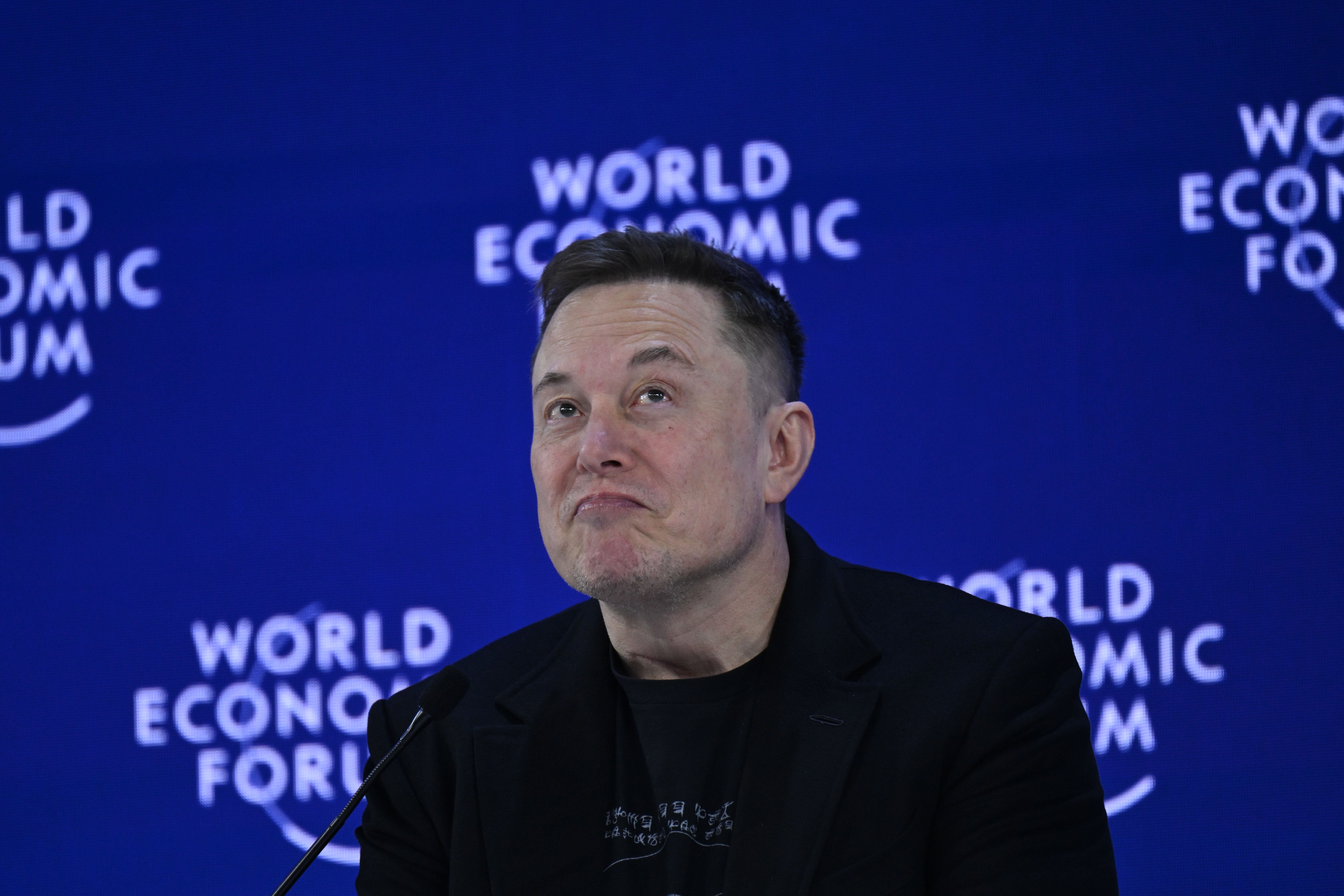 En person i mørk blazer taler på scenen i World Economic Forum, med et gjennomtenkt uttrykk
