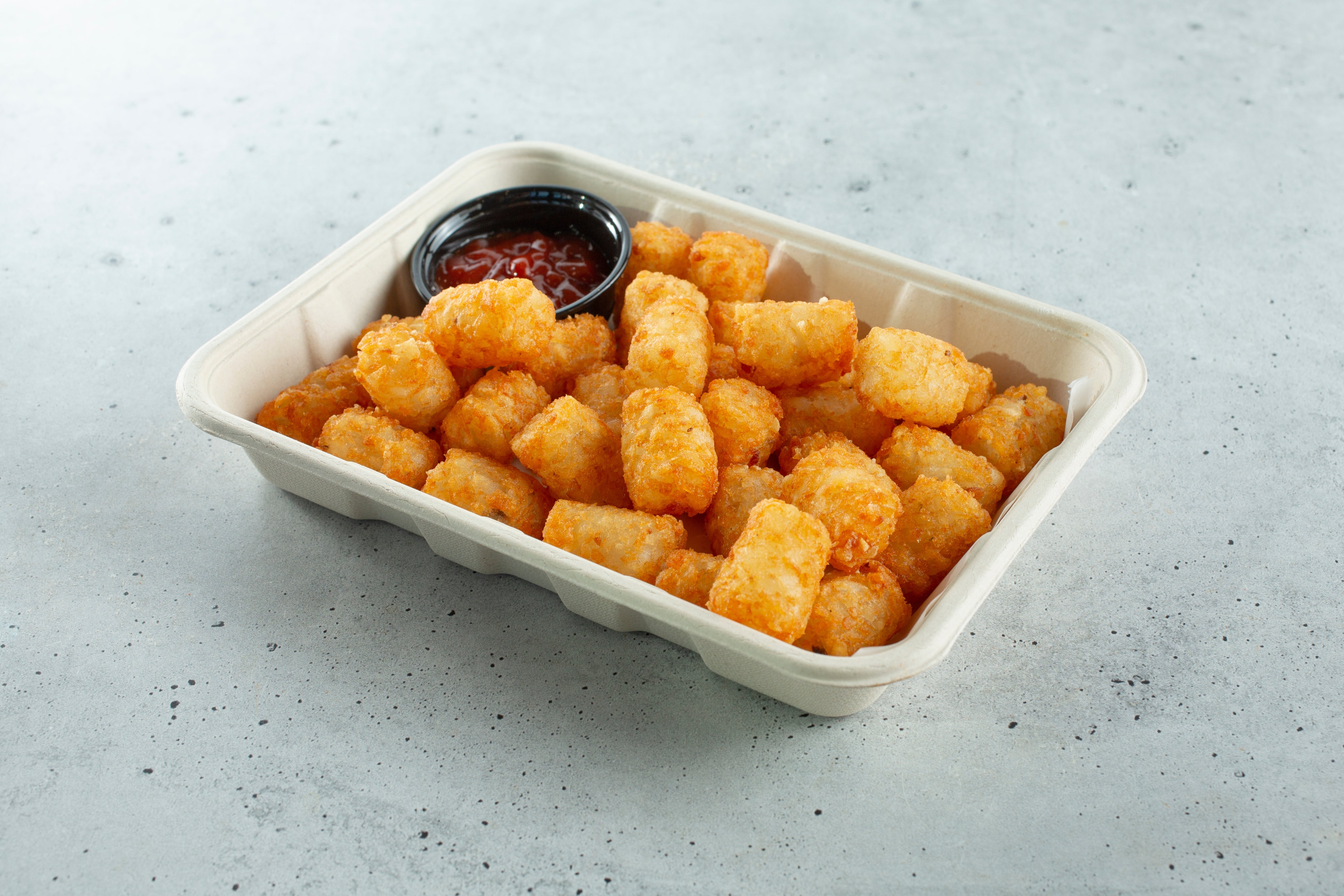 Tray of crispy tater tots with a broadside of ketchup for dipping connected a textured surface