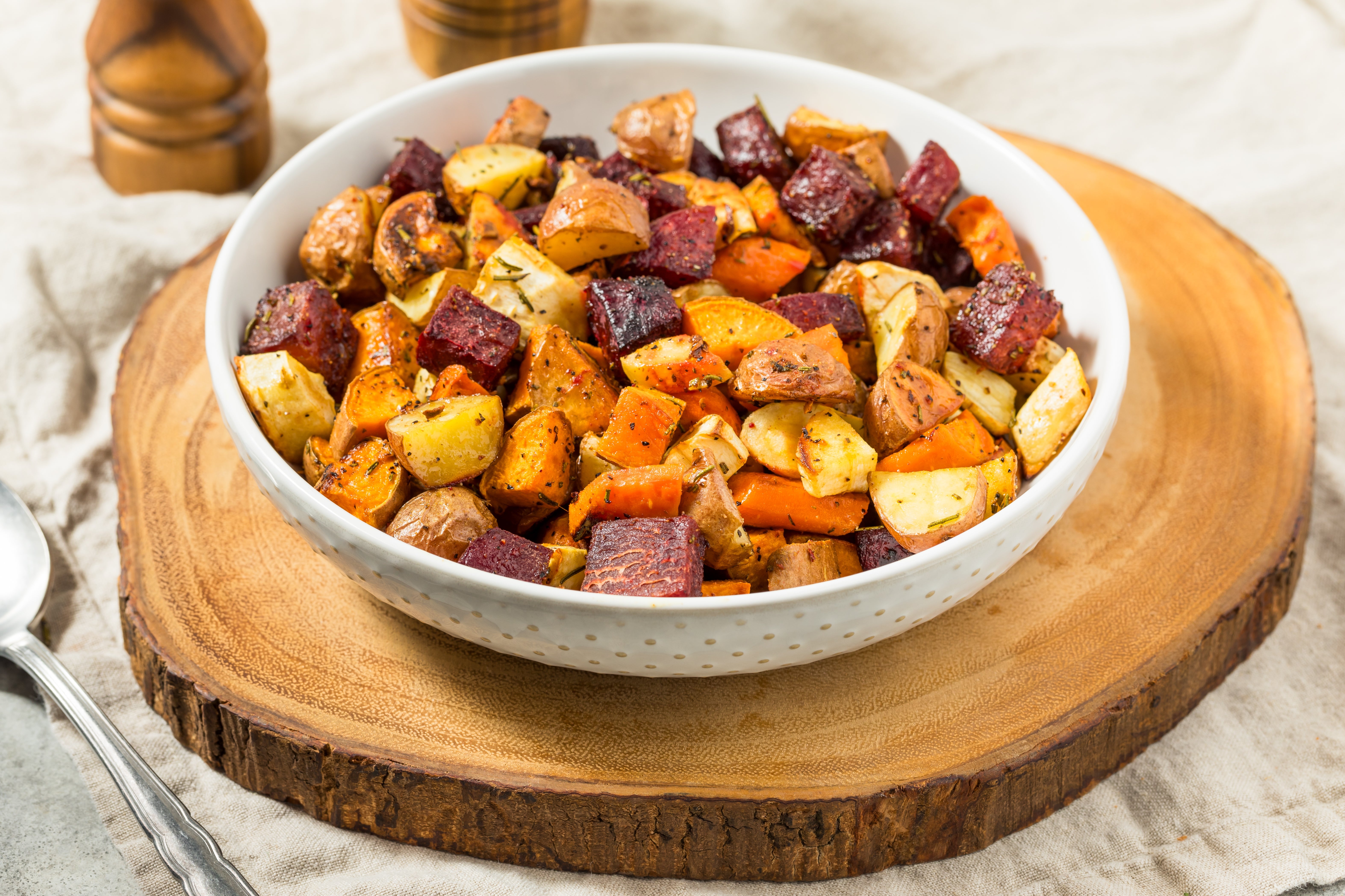 A vessel of roasted basal vegetables, including beets, potatoes, and carrots, seasoned with herbs, placed connected a woody board