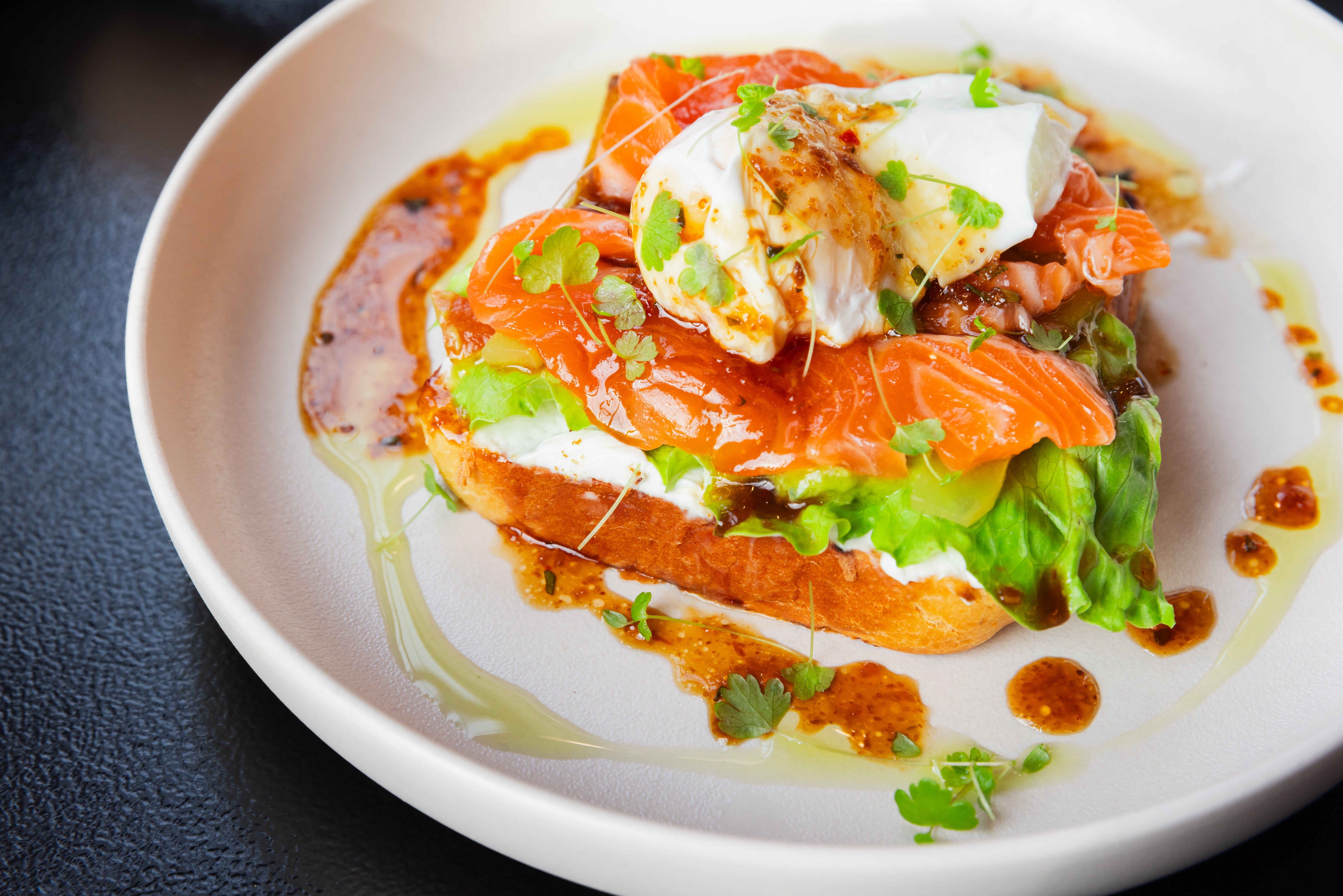Open-faced sandwich with smoked salmon, poached egg, lettuce, and dressing connected a achromatic plate
