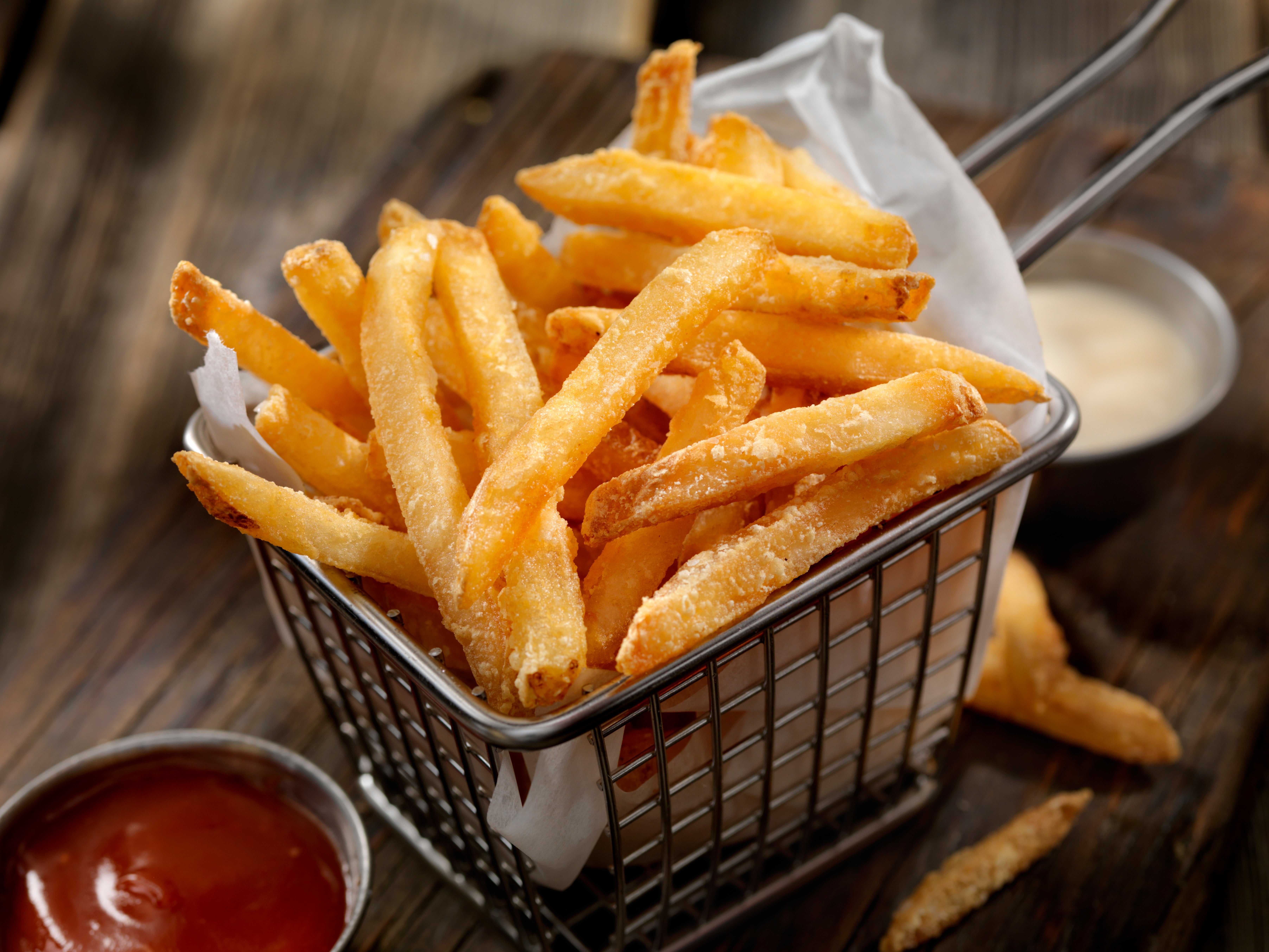 Basket of crispy French fries with dips connected a woody table