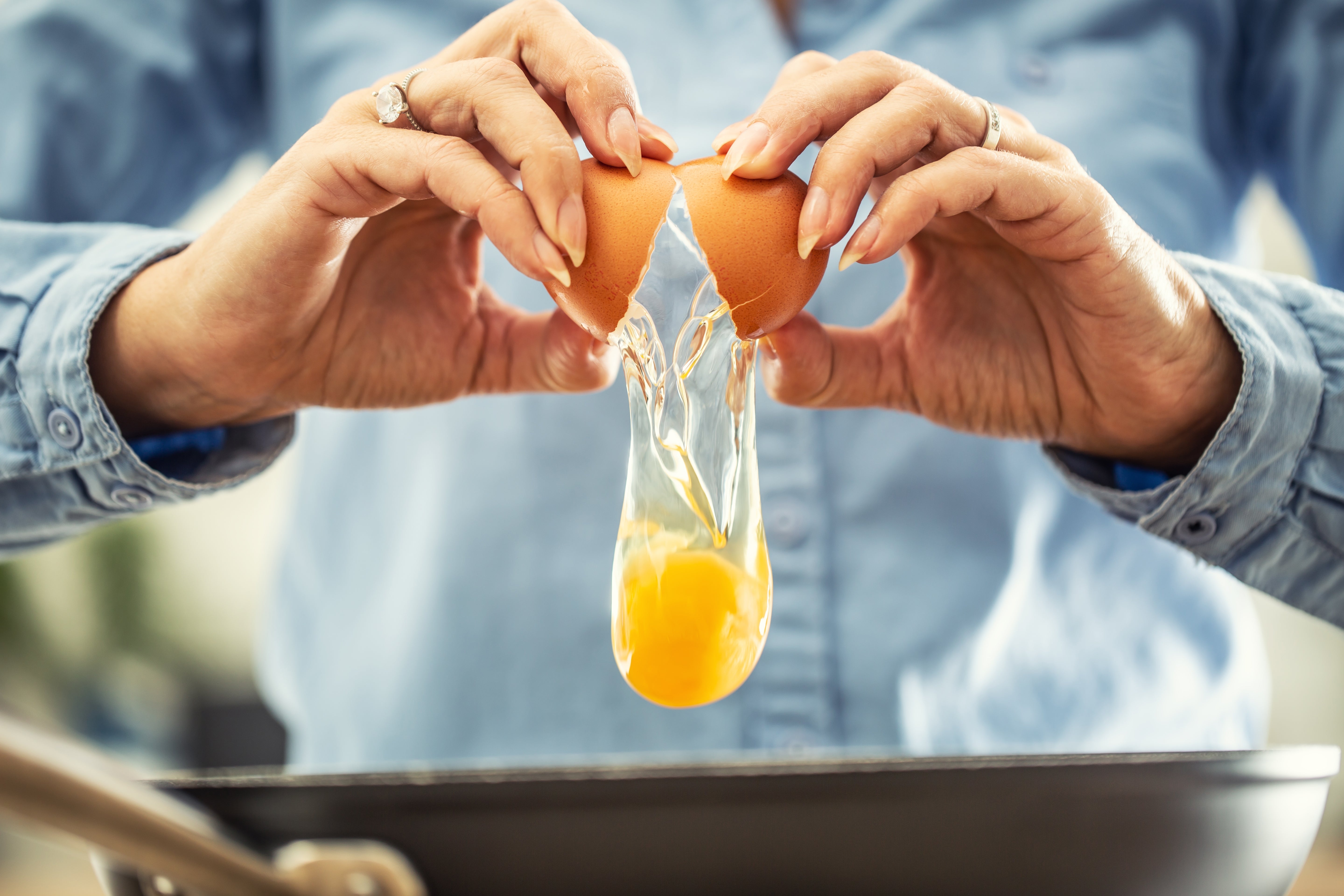 Close-up of hands cracking an ovum implicit a frying pan, yolk disposable mid-air