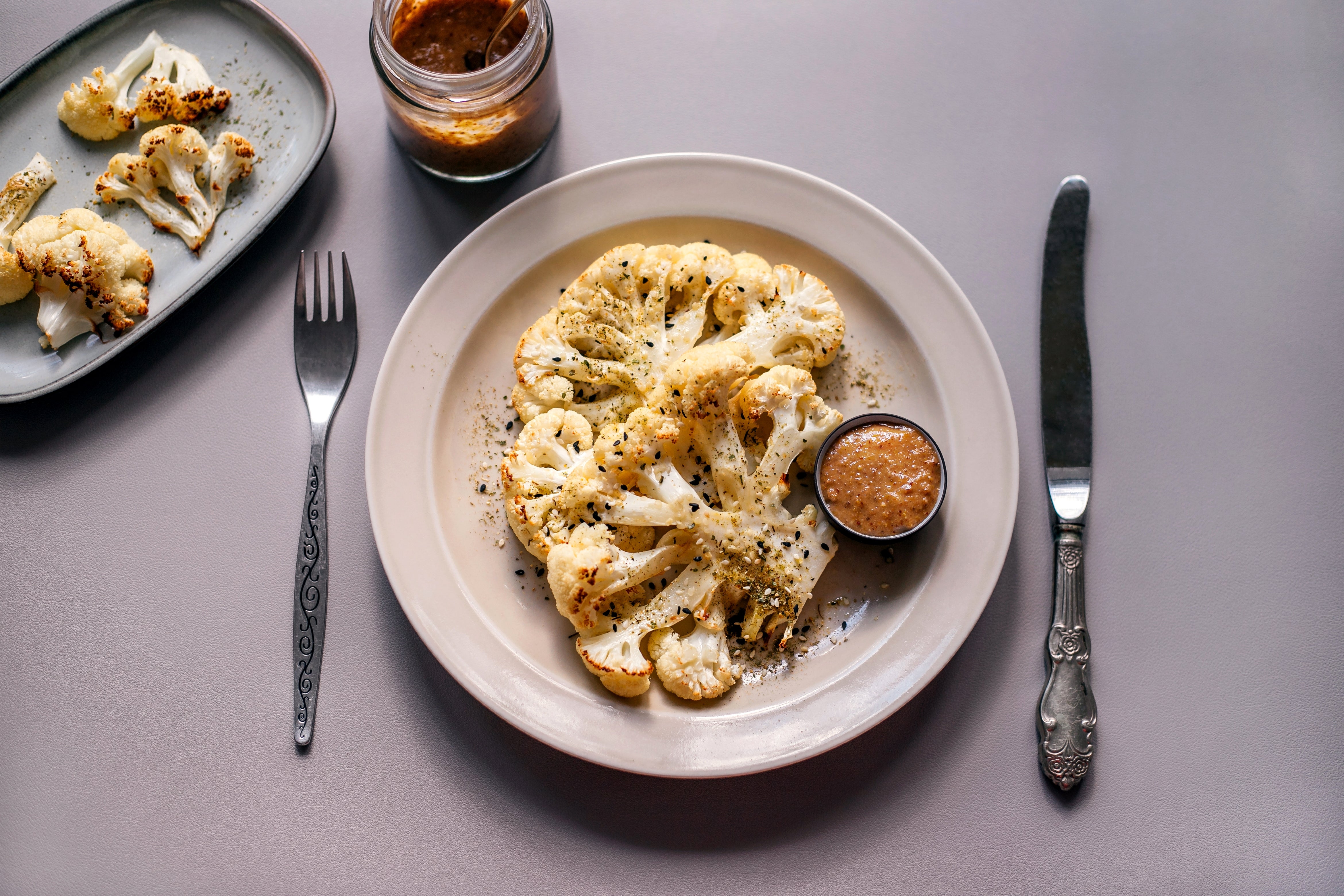 Roasted cauliflower steak with herbs connected a plate, accompanied by a tiny crockery of dipping sauce. A fork and weapon are placed beside the plate