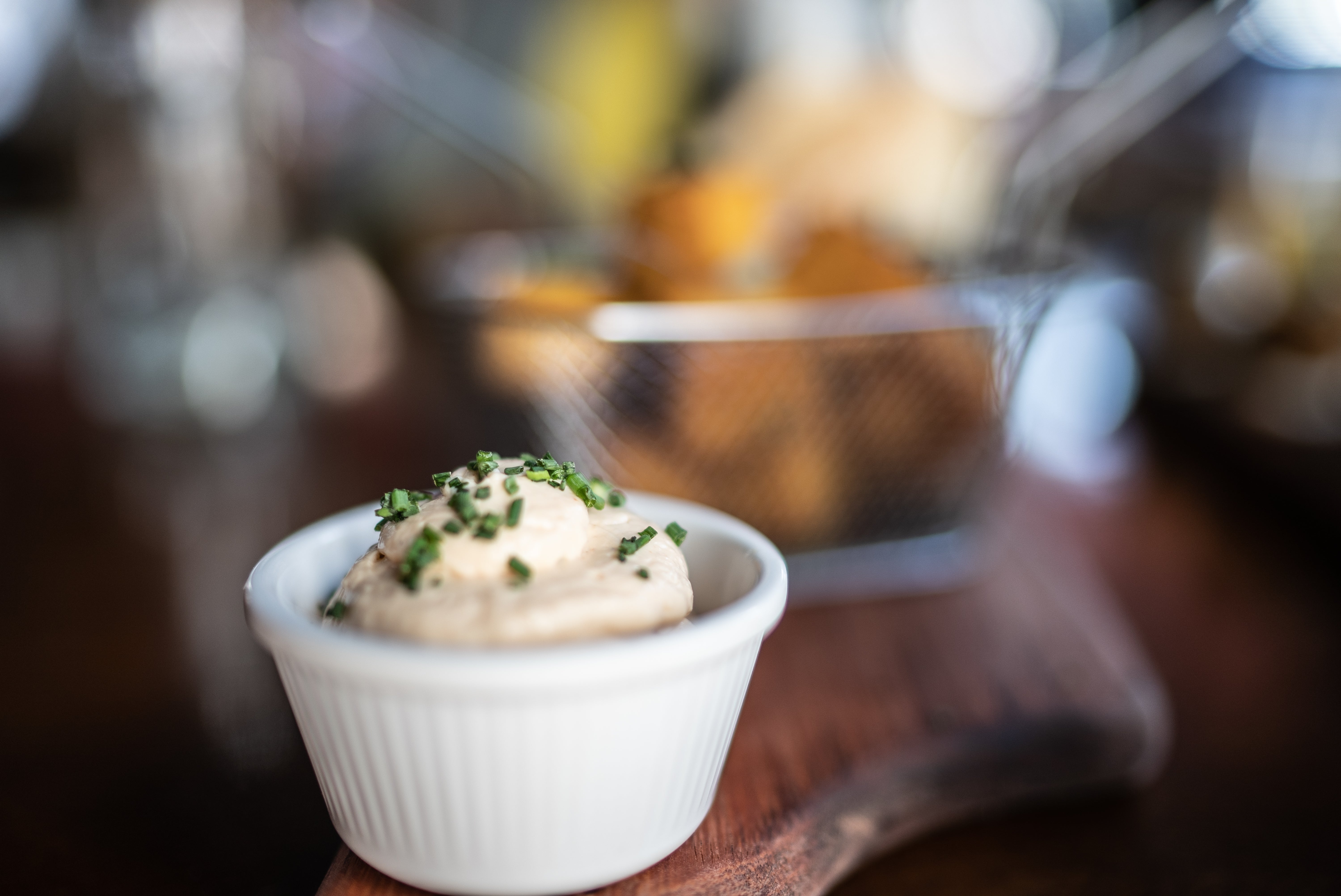 A tiny achromatic crockery of creamy dip topped with chopped herbs, placed connected a woody board, with a blurred handbasket of nutrient successful the background