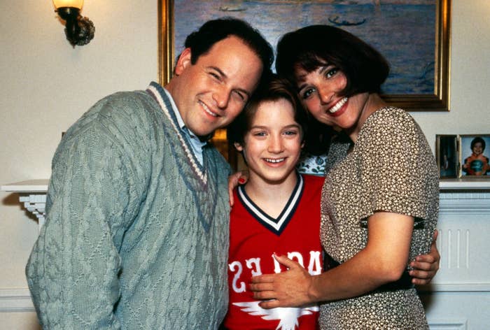 Three radical   basal   intimately  together, smiling warmly. The antheral   wears a sweater, the pistillate   wears a patterned dress, and the kid  sports a sports jersey