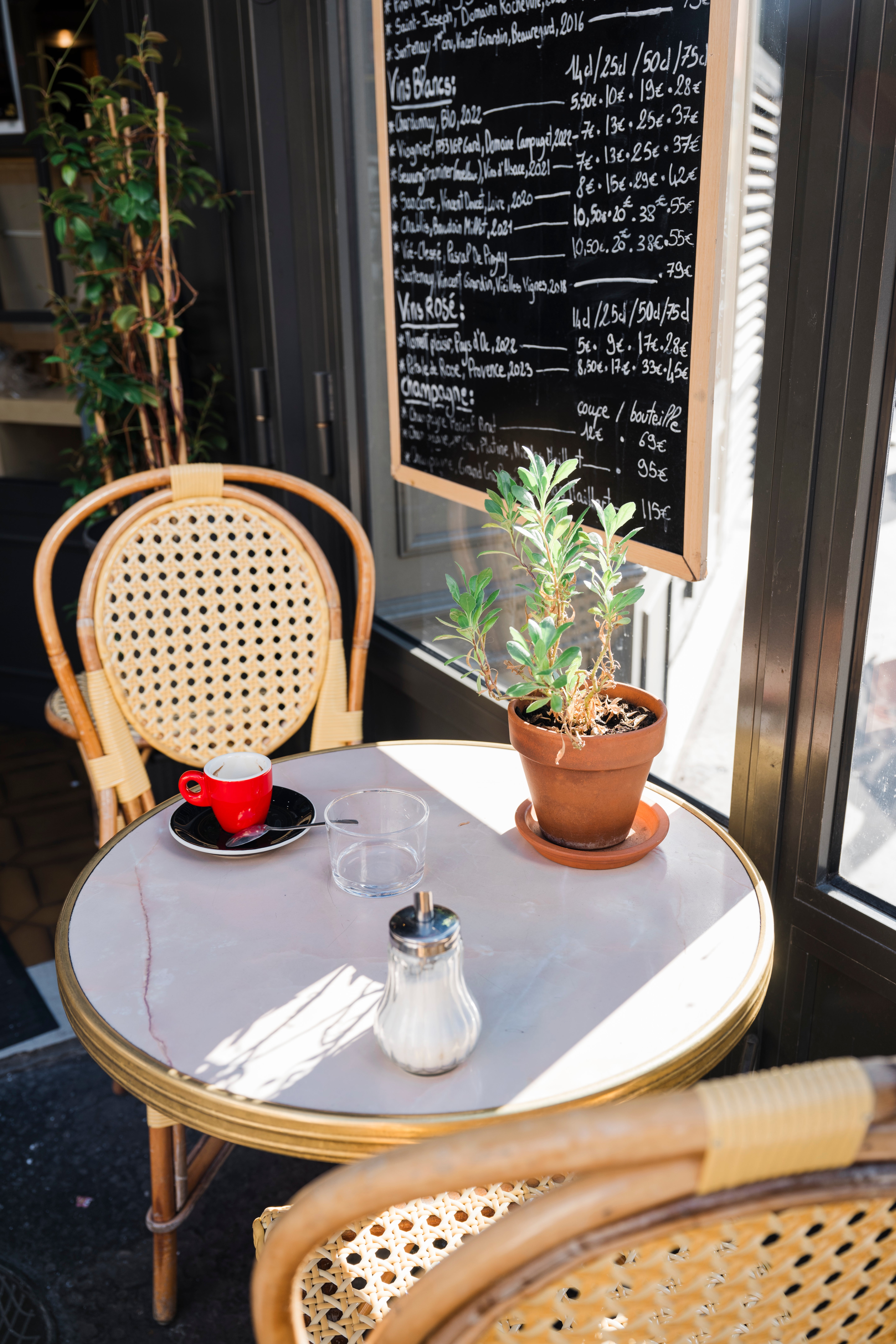 Outdoor cafe array with a reddish java cup, glass, sweetener dispenser, and potted plant; chalkboard paper successful the background