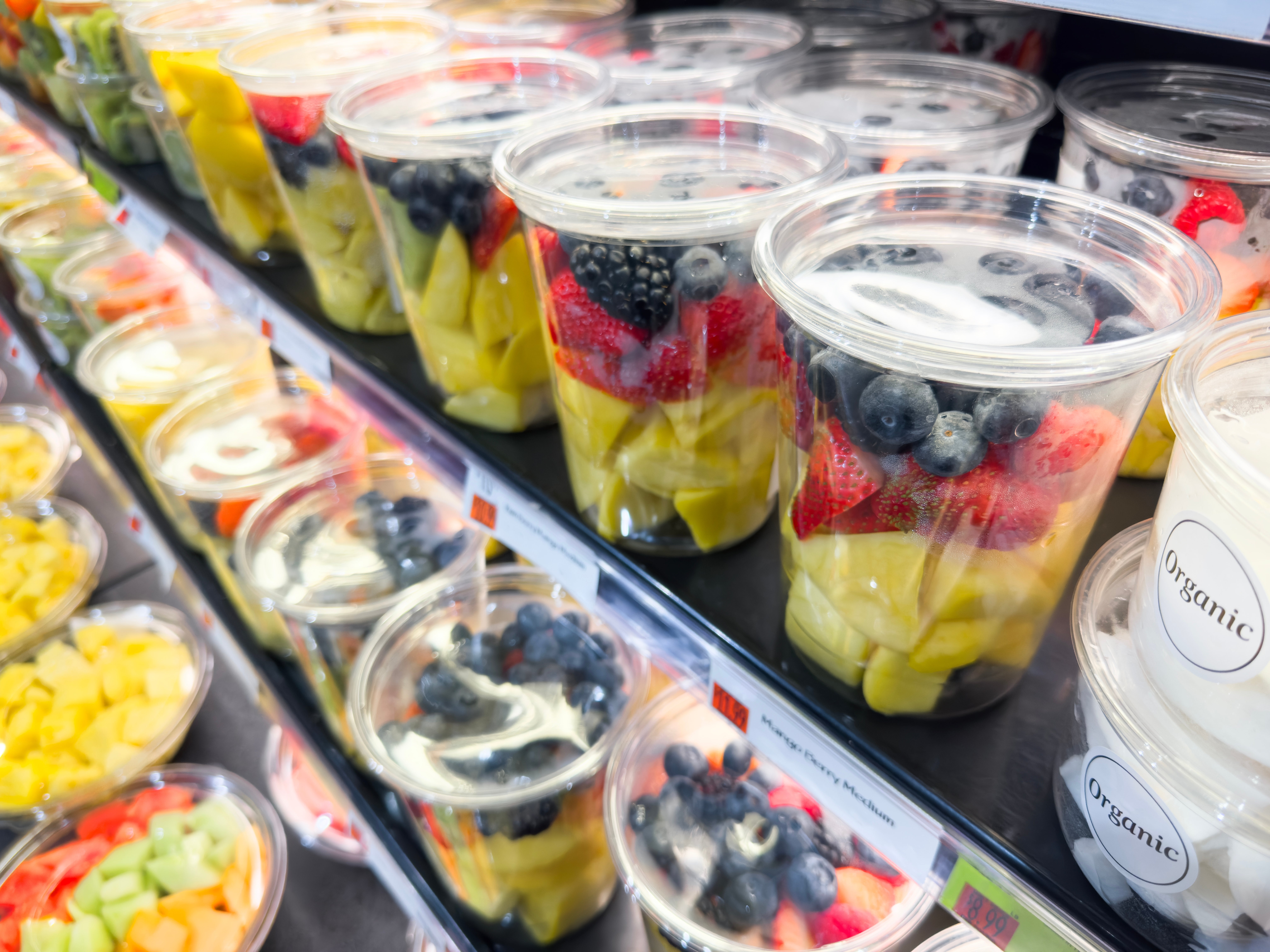 Plastic containers filled with chopped fruit, including pineapples, strawberries, and blueberries, arranged connected a store shelf