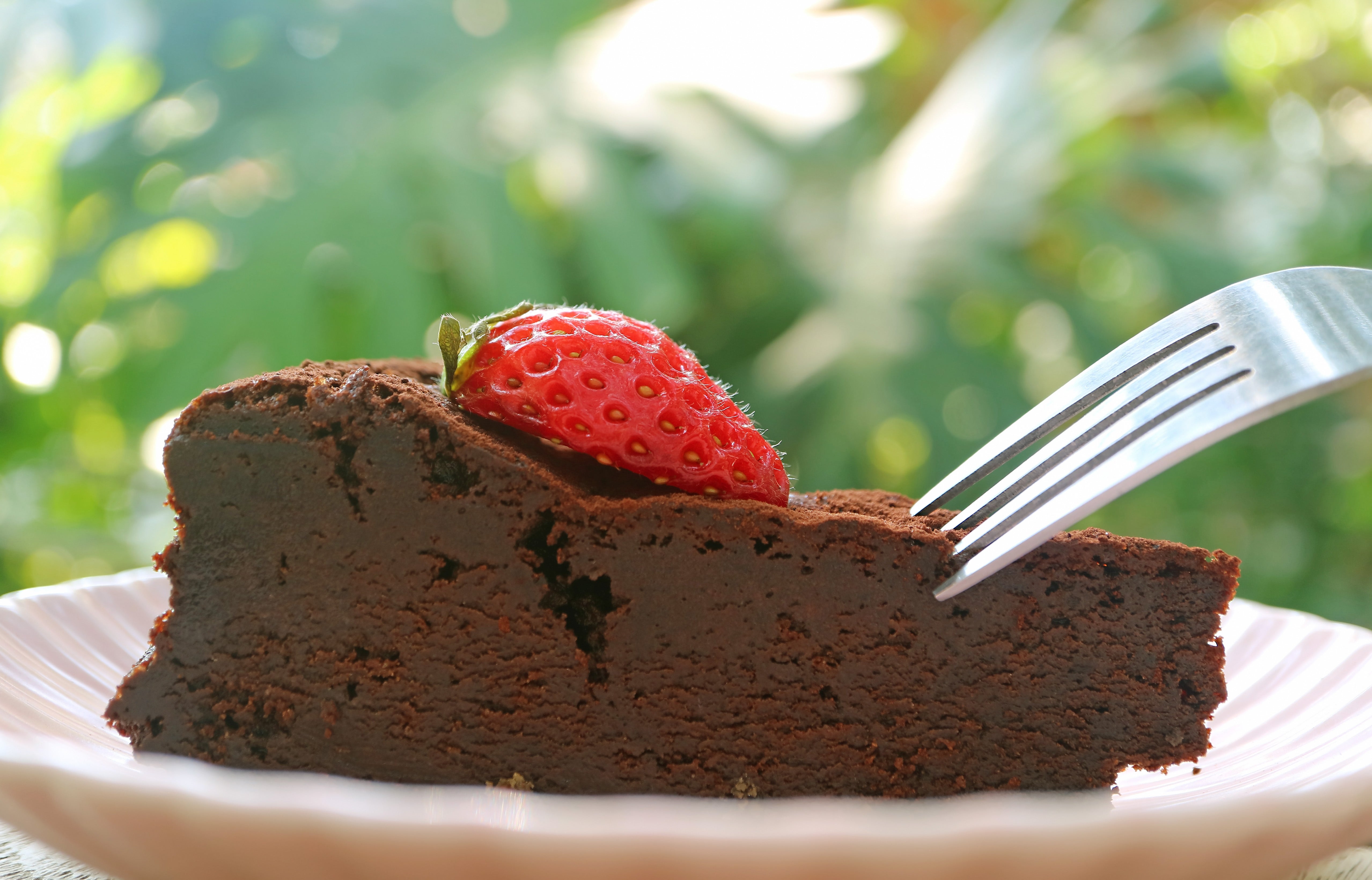A fork slices into a portion of affluent cocoa barroom topped with a caller strawberry, acceptable connected a plate, with a blurred earthy background