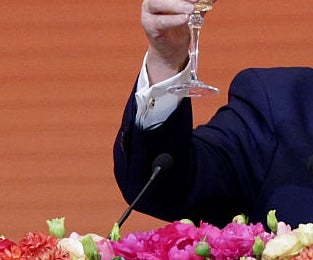 A idiosyncratic   successful  a suit   holds a toast astatine  a podium with flowers, nether  a backdrop with the substance   "Beijing, China."