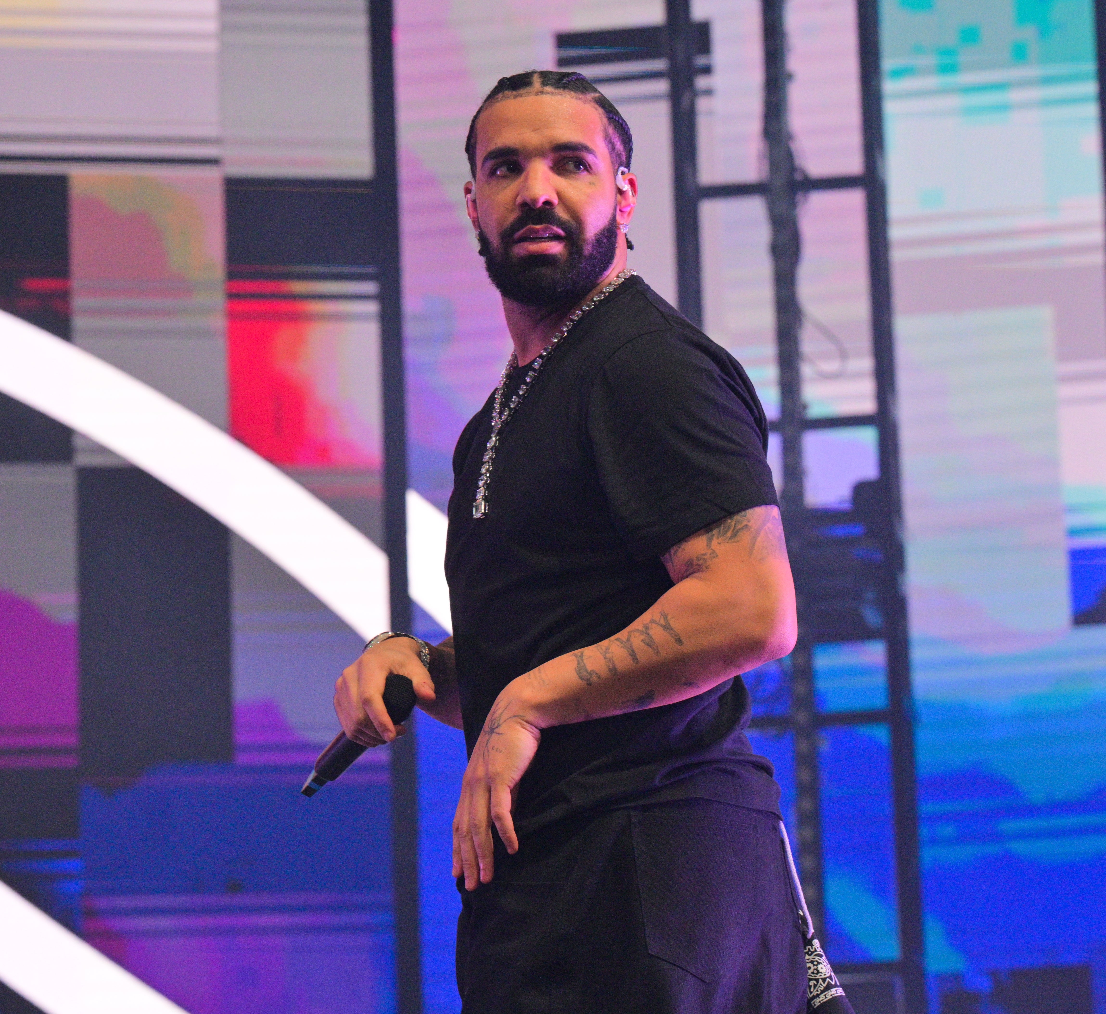 Drake on stage in casual attire, holding a microphone, with a geometric background display
