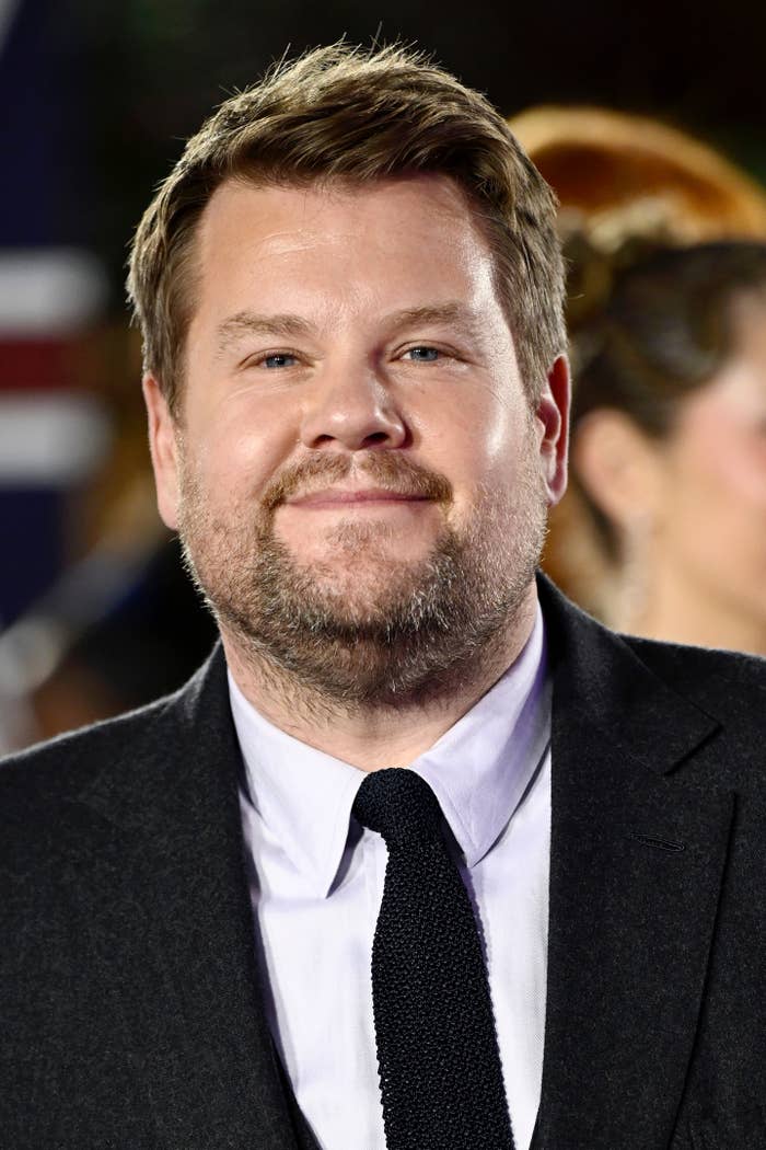James Corden in a suit and tie smiles at a formal event