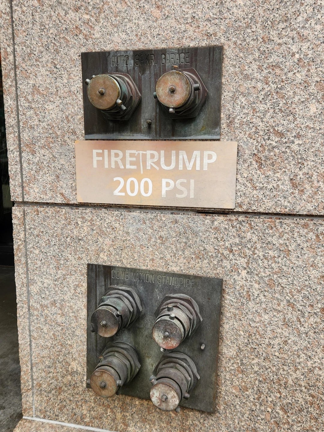 Fire hydrant connections on a wall, labeled "FIRE TRUMP 200 PSI," combining humor with infrastructure signage