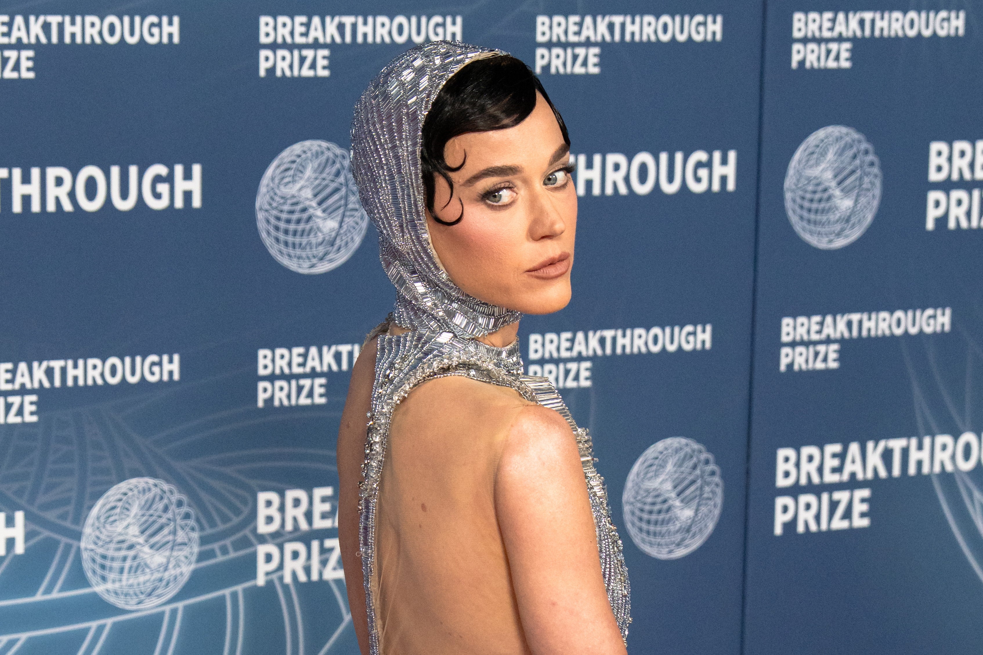 Katy Perry in stylish backless outfit with jeweled headpiece at Breakthrough Prize event backdrop