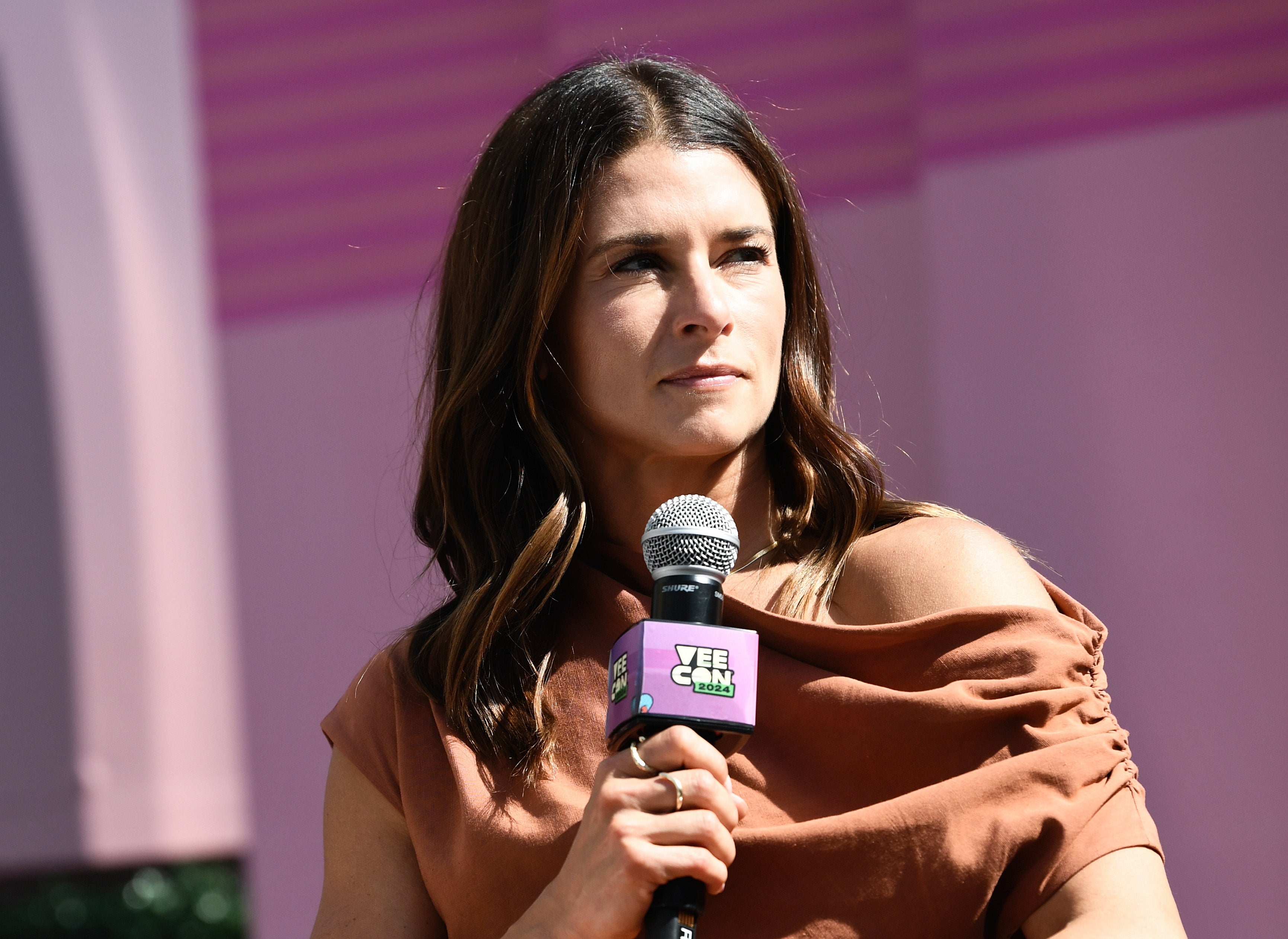 Danica Patrick holds a microphone at an event, wearing an off-shoulder top