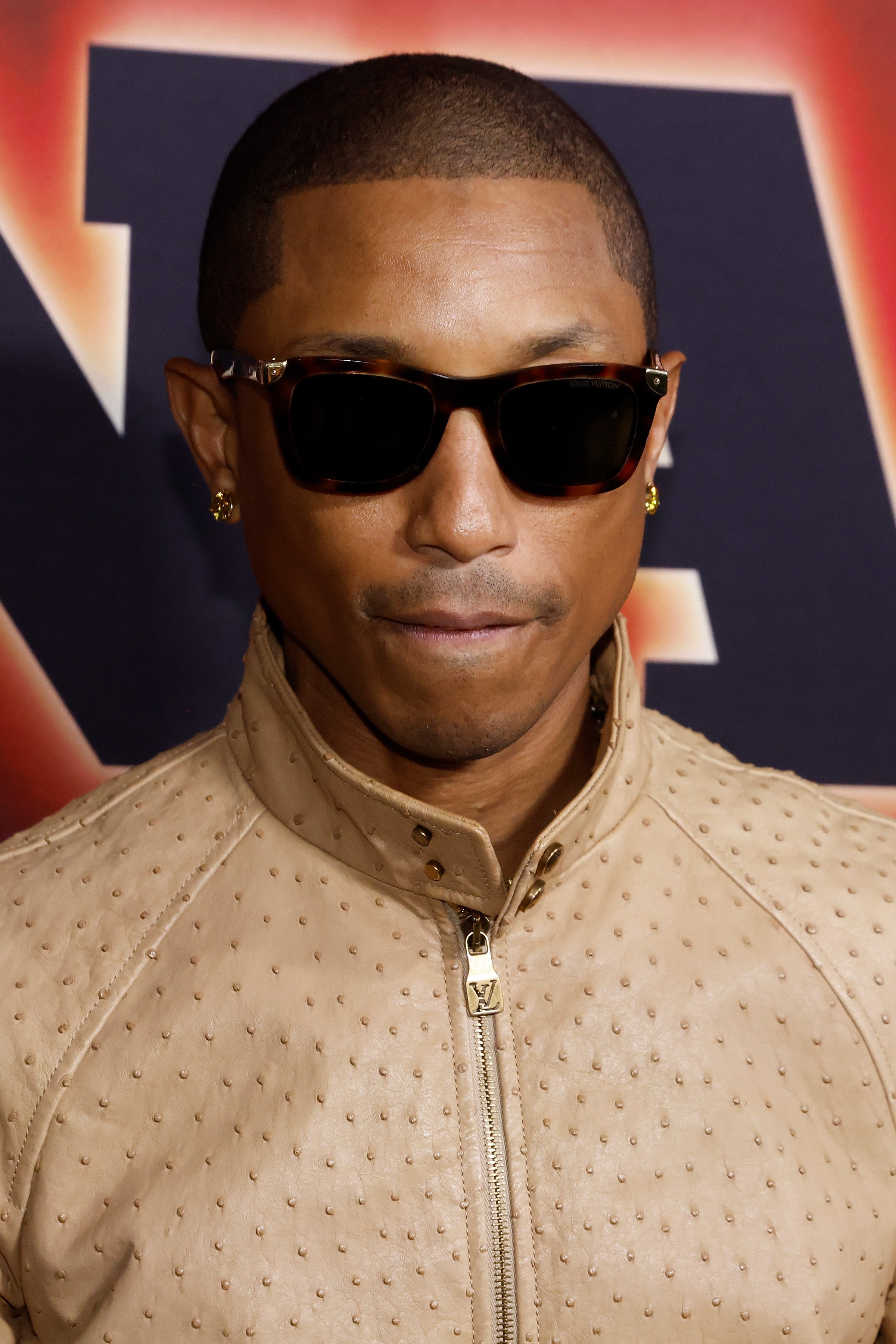 Pharrell wearing sunglasses and a sleek, textured jacket at an event
