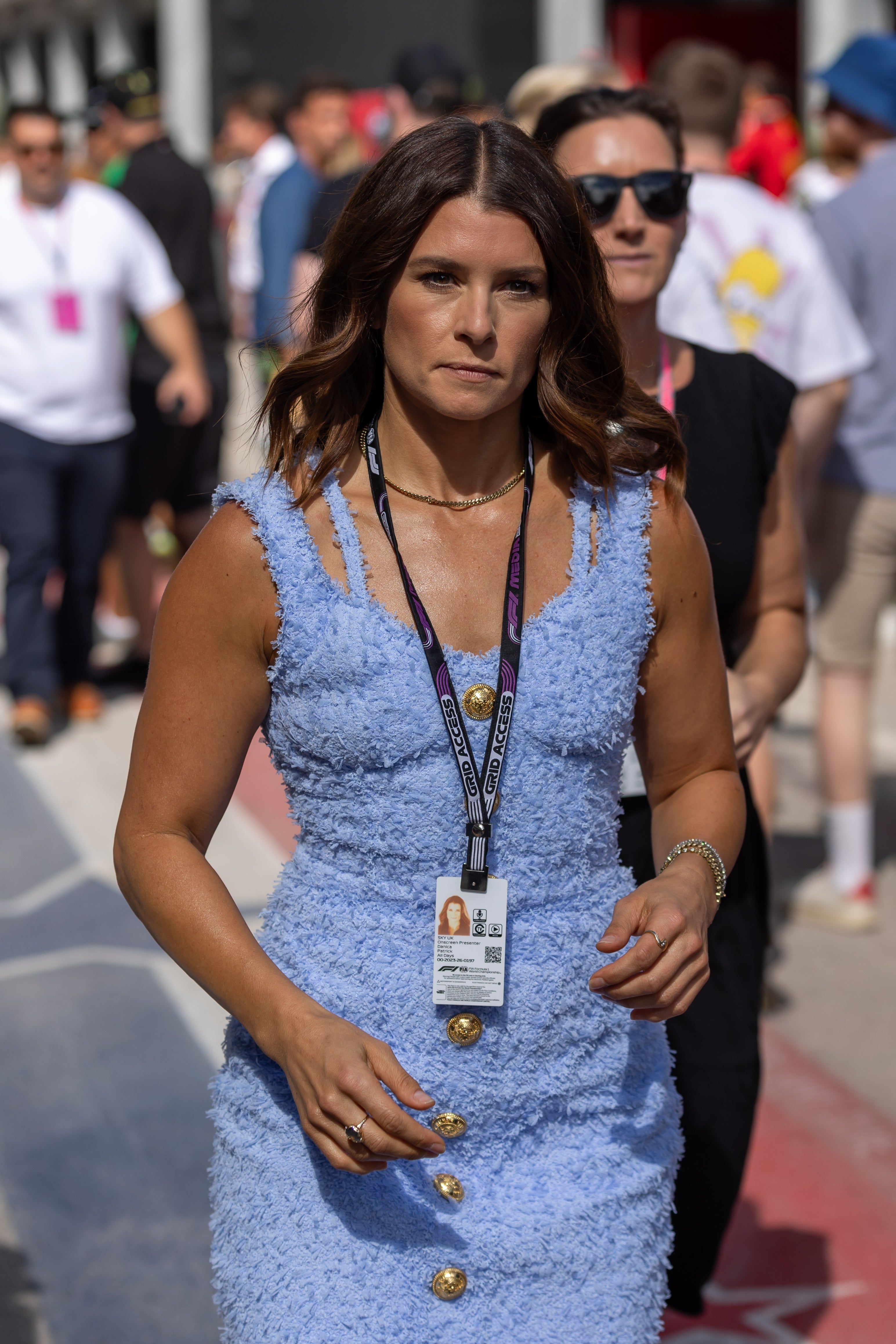 Danica Patrick in textured dress walking outdoors, wearing an event badge and necklace, flanked by others in background