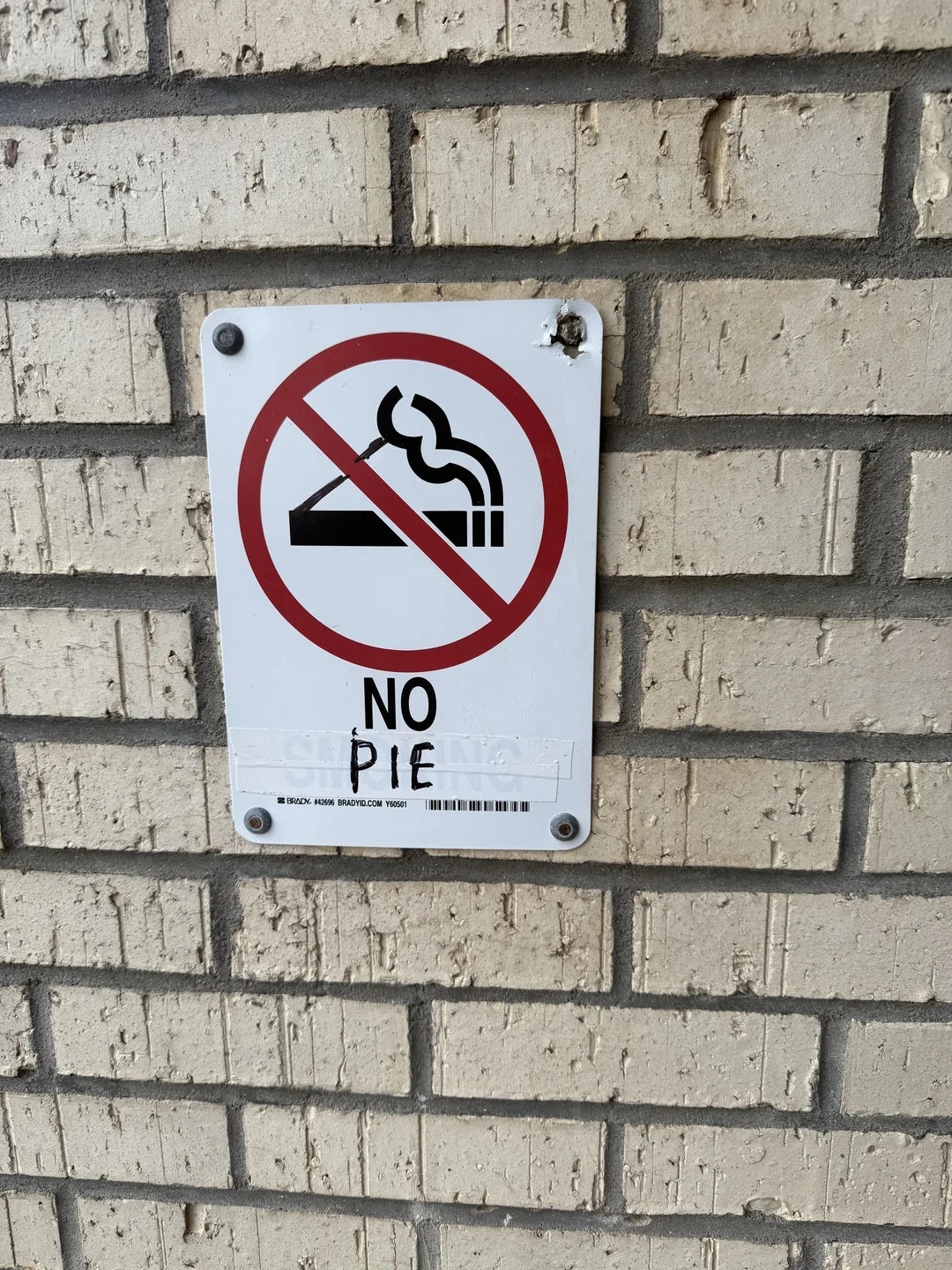 Sign on a brick wall with a crossed-out pie symbol reads "No Pie," humorously indicating a restriction on pies