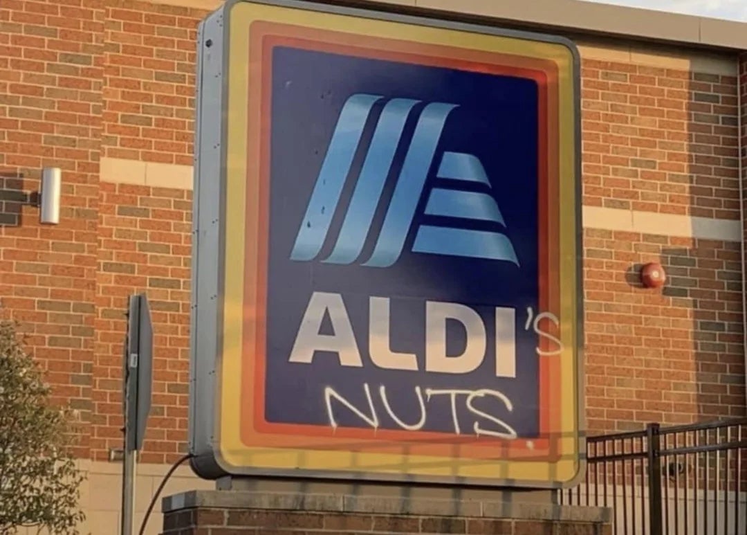 A graffiti on an ALDI store sign adds the word "NUTS" humorously beneath the logo