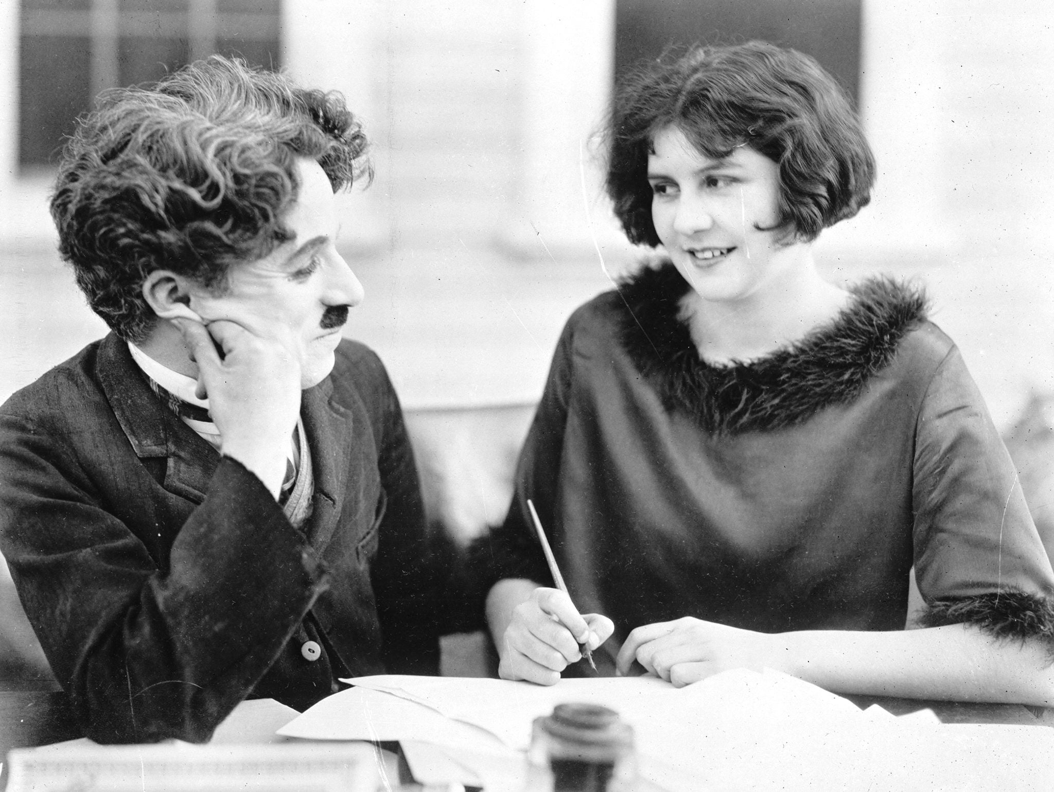 A celebrated soundless movie histrion successful a classical suit shares a lukewarm infinitesimal with a young pistillate holding a pen, some smiling astatine each other