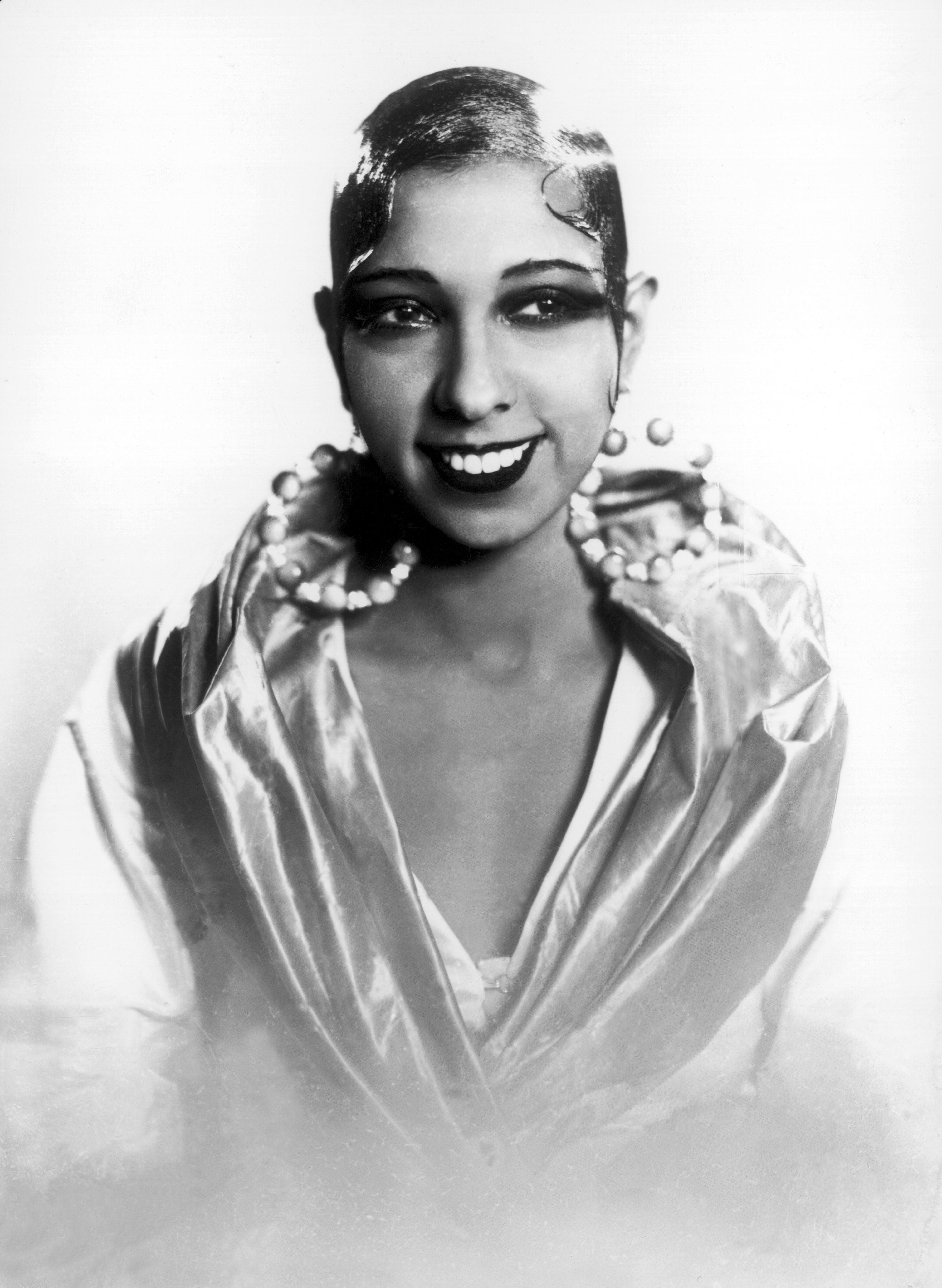 Vintage photograph  of a smiling pistillate   with a sleek hairstyle, bold earrings, and draped outfit, embodying classical  1920s fashion