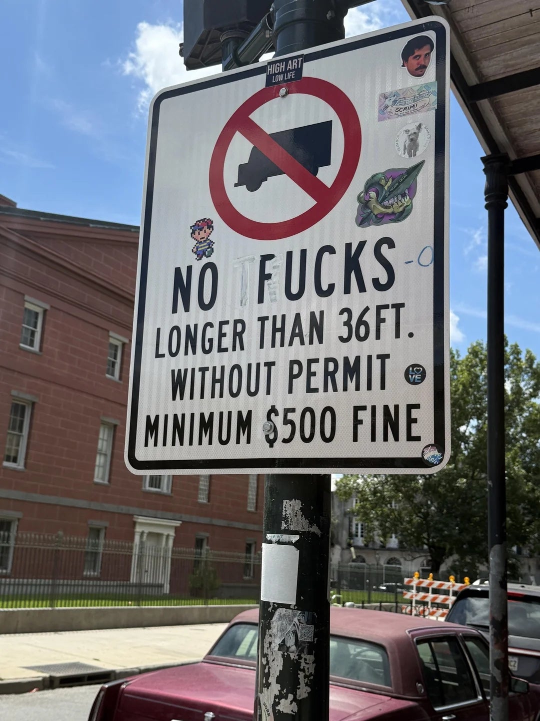 Street sign prohibiting trucks longer than 36 feet without a permit, showing a minimum fine of $500. Stickers decorate the sign