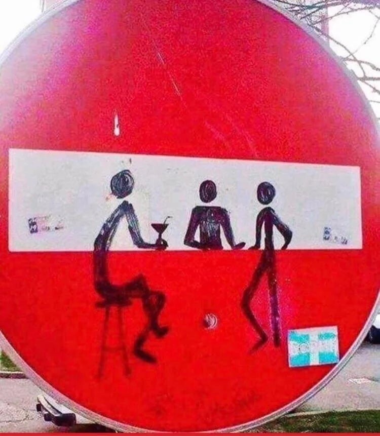 Street art on a round red traffic sign depicts stick figures socializing at a bar, with one holding a drink