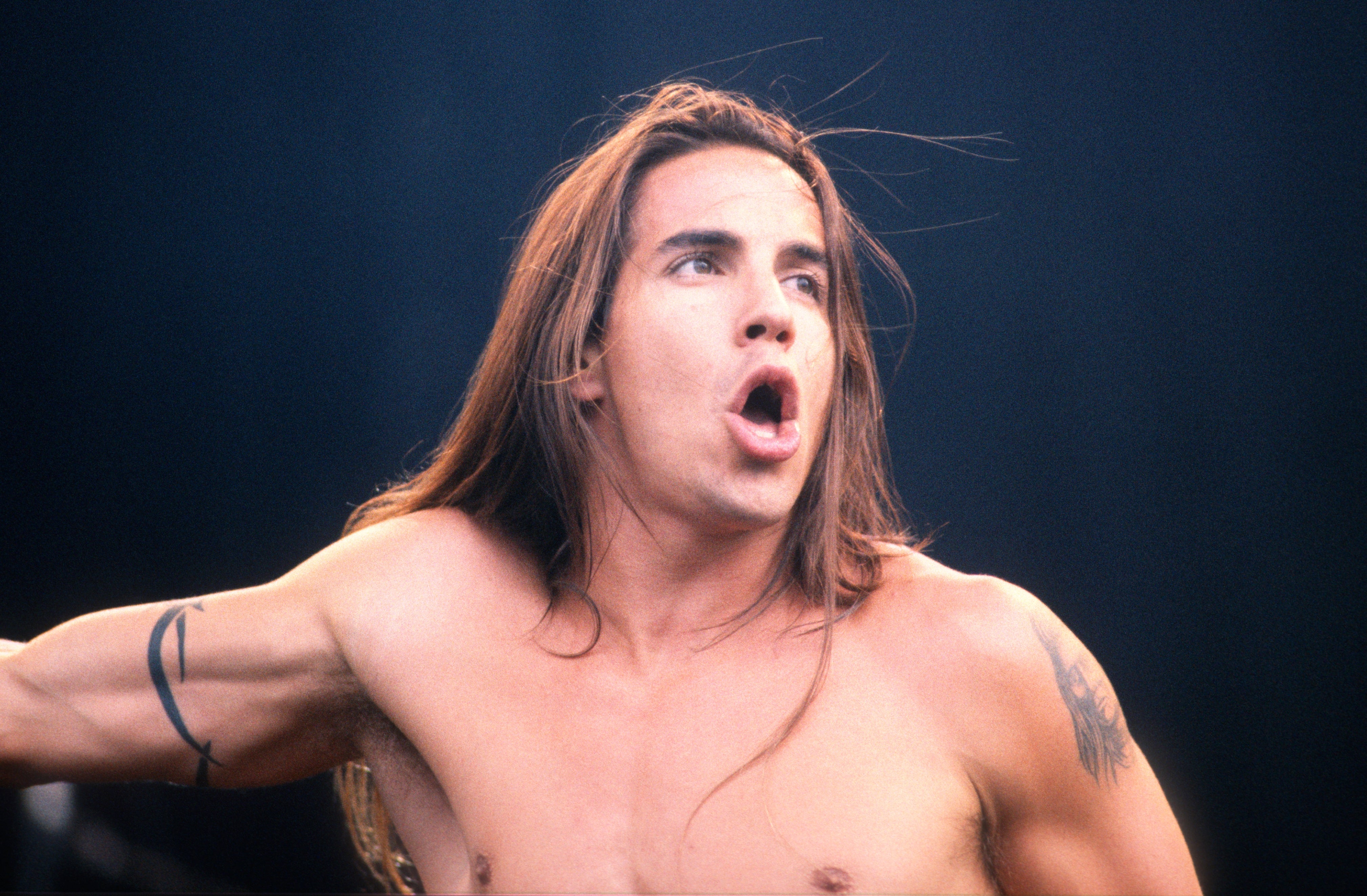 Person performing energetically, wearing nary shirt, with agelong hairsbreadth flowing, conveying strength during a unrecorded show