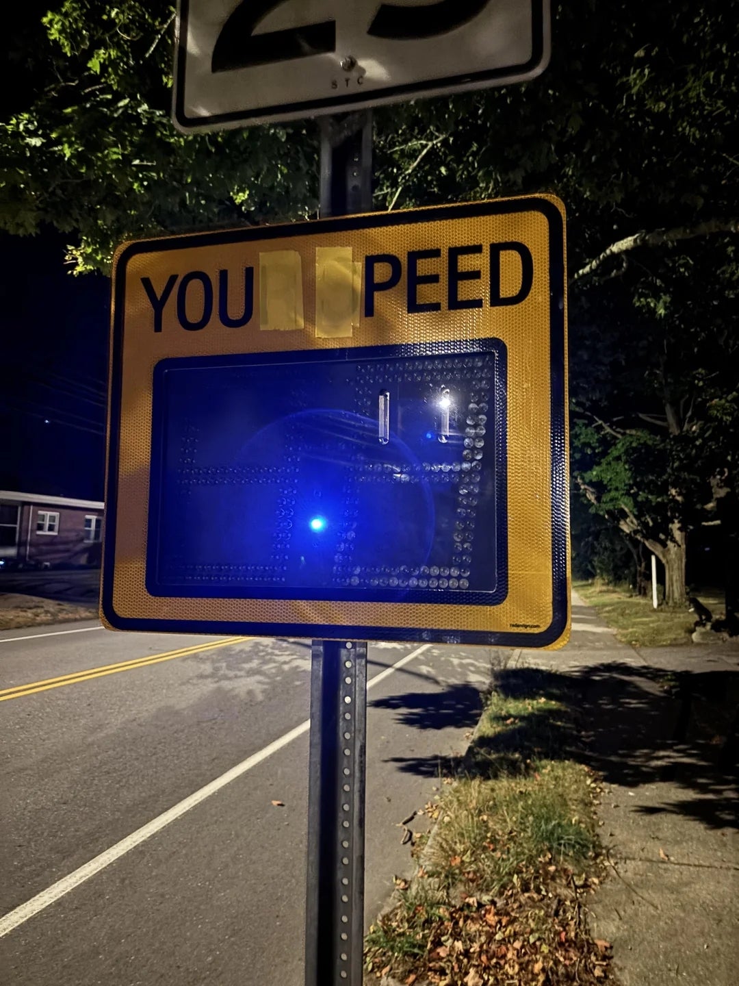 Traffic sign at night with letters partially obscured, making it read "YOU PEED."