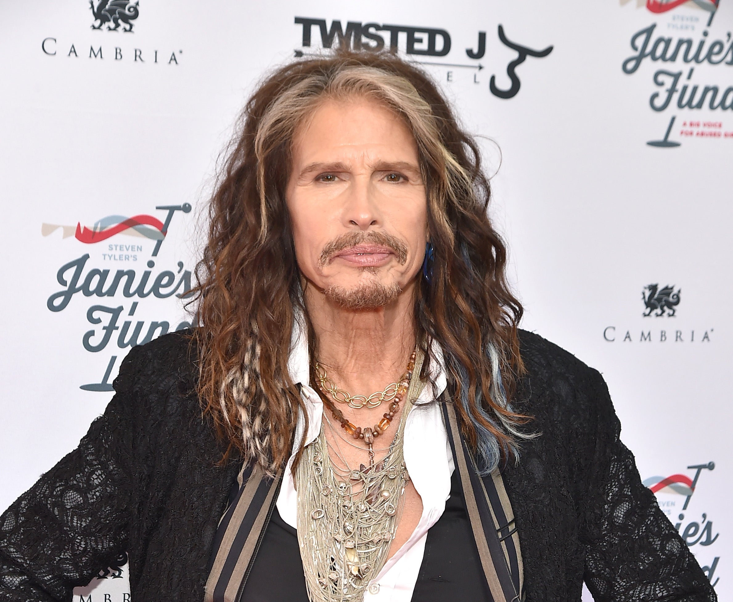A idiosyncratic with agelong hairsbreadth is connected a reddish carpet, wearing layered necklaces and a blazer implicit a patterned shirt