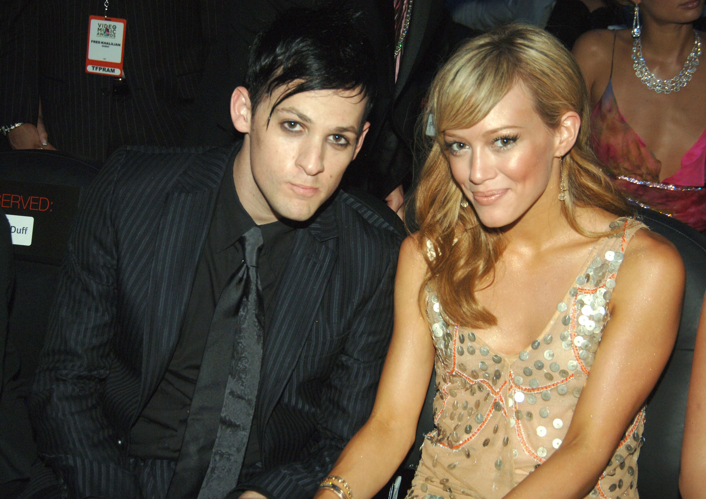 Two radical sitting together; 1 successful a pinstripe suit, the different successful a sequined dress, attending a ceremonial event