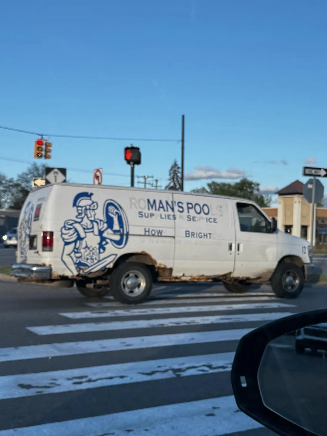 Van with company logo and text, "RO MAN'S POO SUP LIES SERVICE," parked at an intersection. Rust visible on the lower part of the van