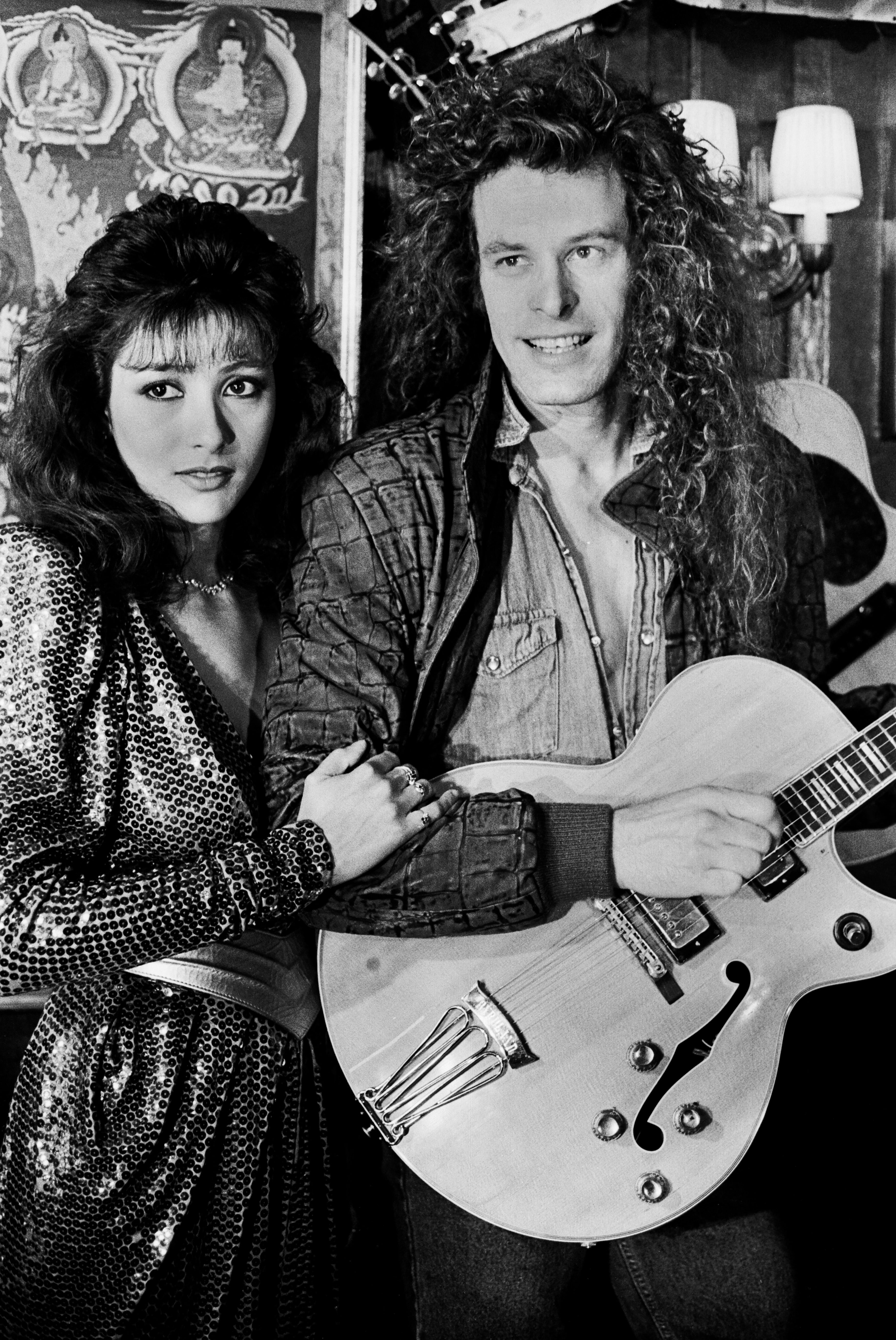 Two individuals successful a vintage photo. The idiosyncratic connected the close holds a guitar, portion the near idiosyncratic wears a shimmering outfit with puffed shoulders