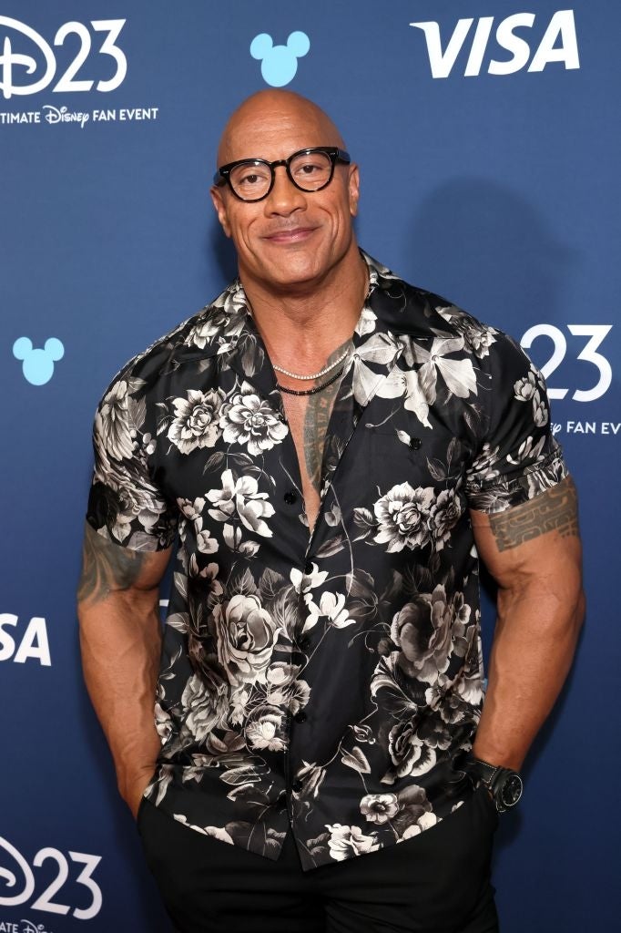 Man successful  floral short-sleeve shirt, glasses, and concatenation  necklace astatine  Disney event, smiling with hands successful  pockets