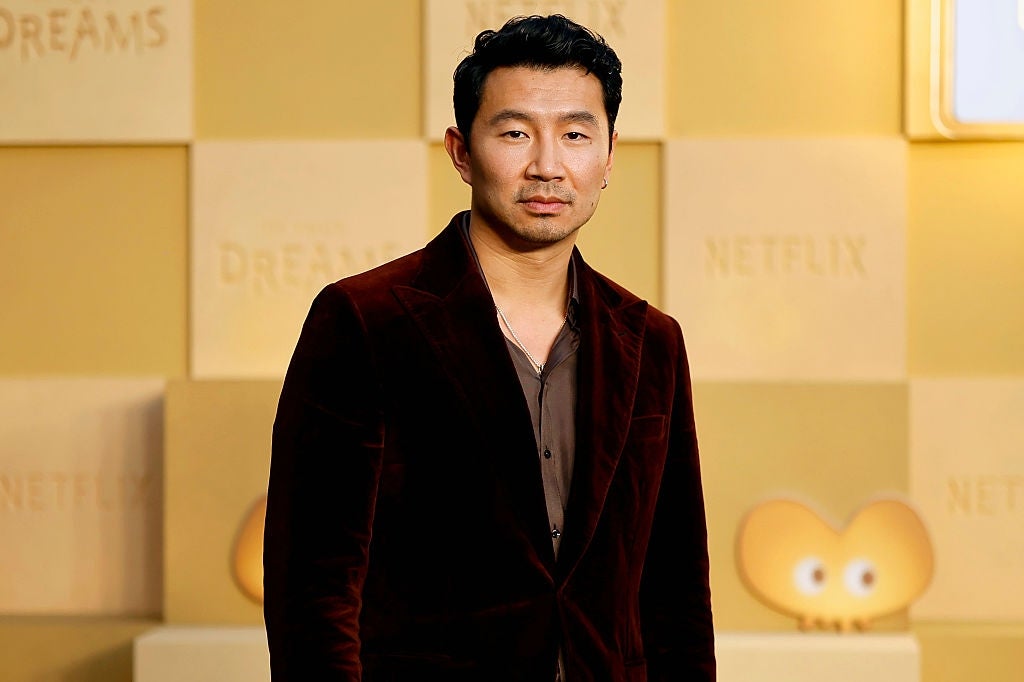 Person successful  a velvet suit   astatine  a media event, lasting  successful  beforehand   of a backdrop with logos and designs