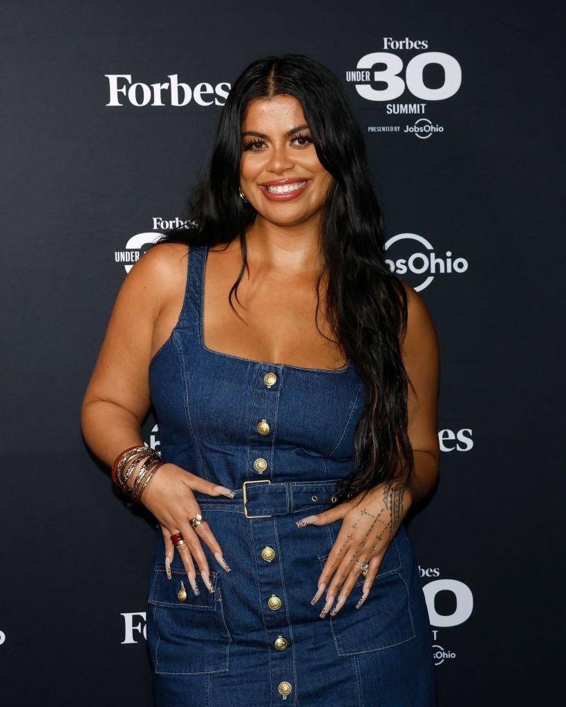 Person successful  a stylish denim formal  with fastener  details poses astatine  a Forbes Under 30 lawsuit   backdrop, smiling and exuding confidence