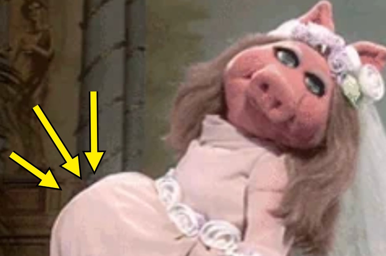 A well-known pig puppet character poses humorously with a fake baby bump, wearing a bridal gown with floral accents