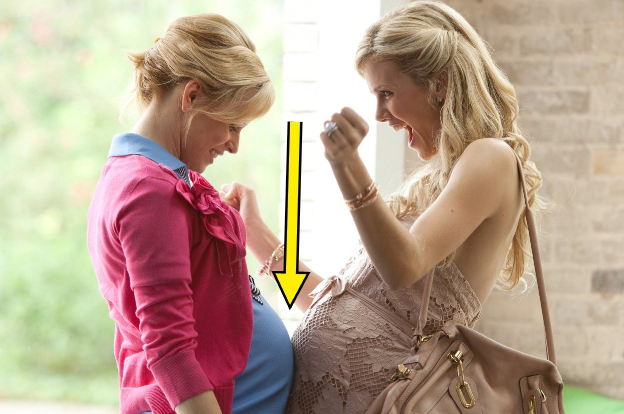 Two women smiling and pointing at each other's pregnant bellies, sharing a joyful moment